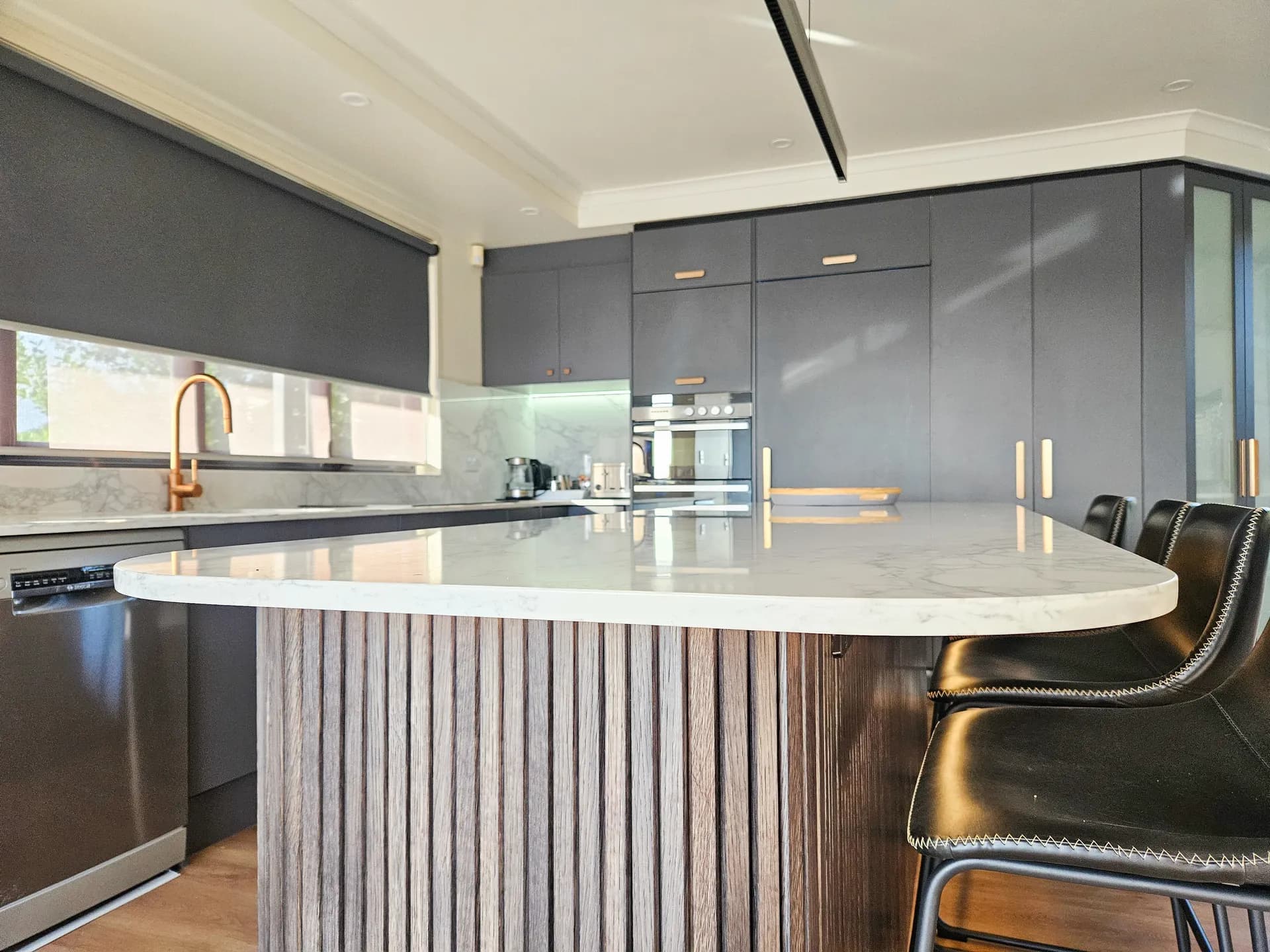 Curved end of a fluted timber-look island with a stone-look benchtop