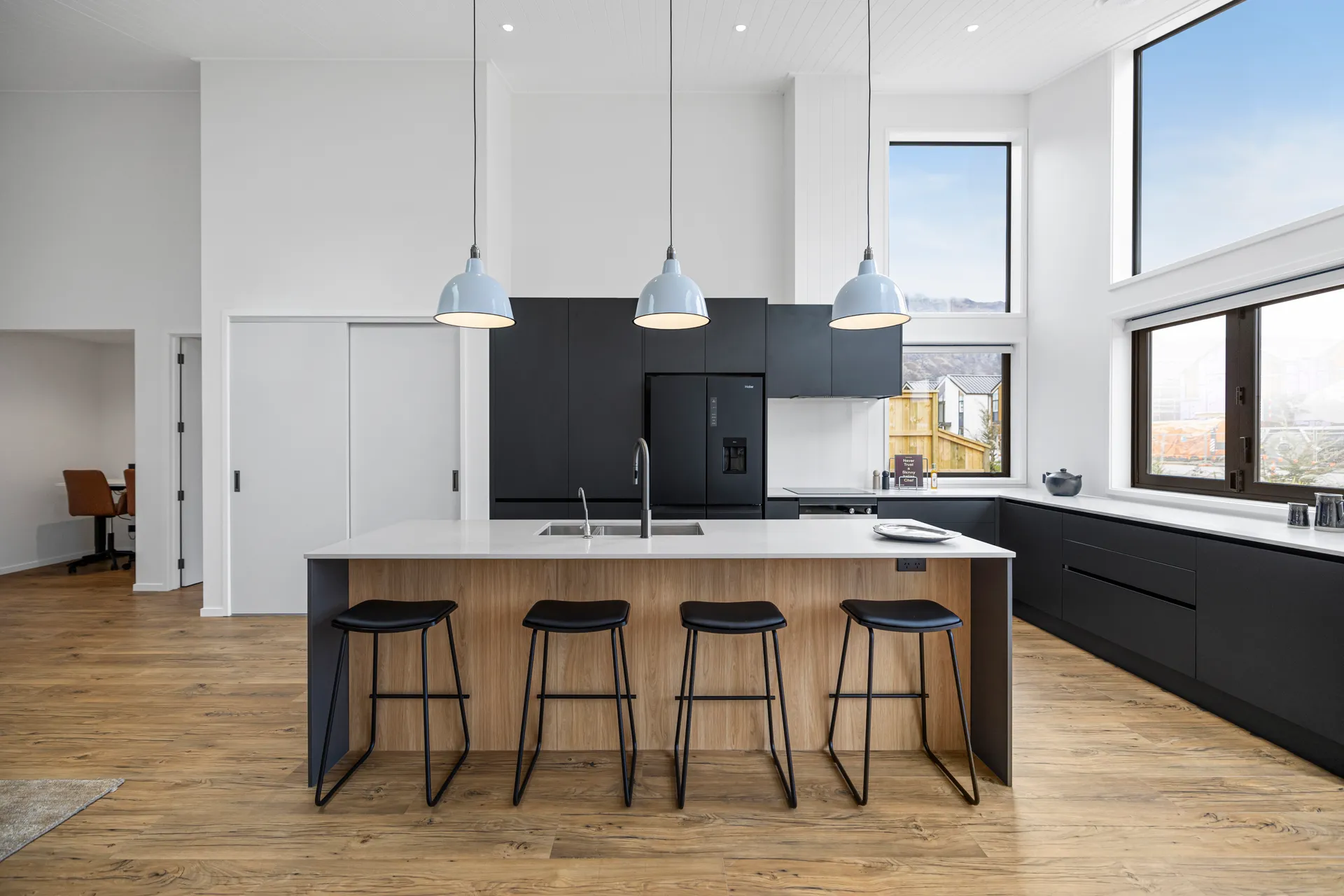 Timber-look island with four black stools in front of black cabinetry and pendant lights
