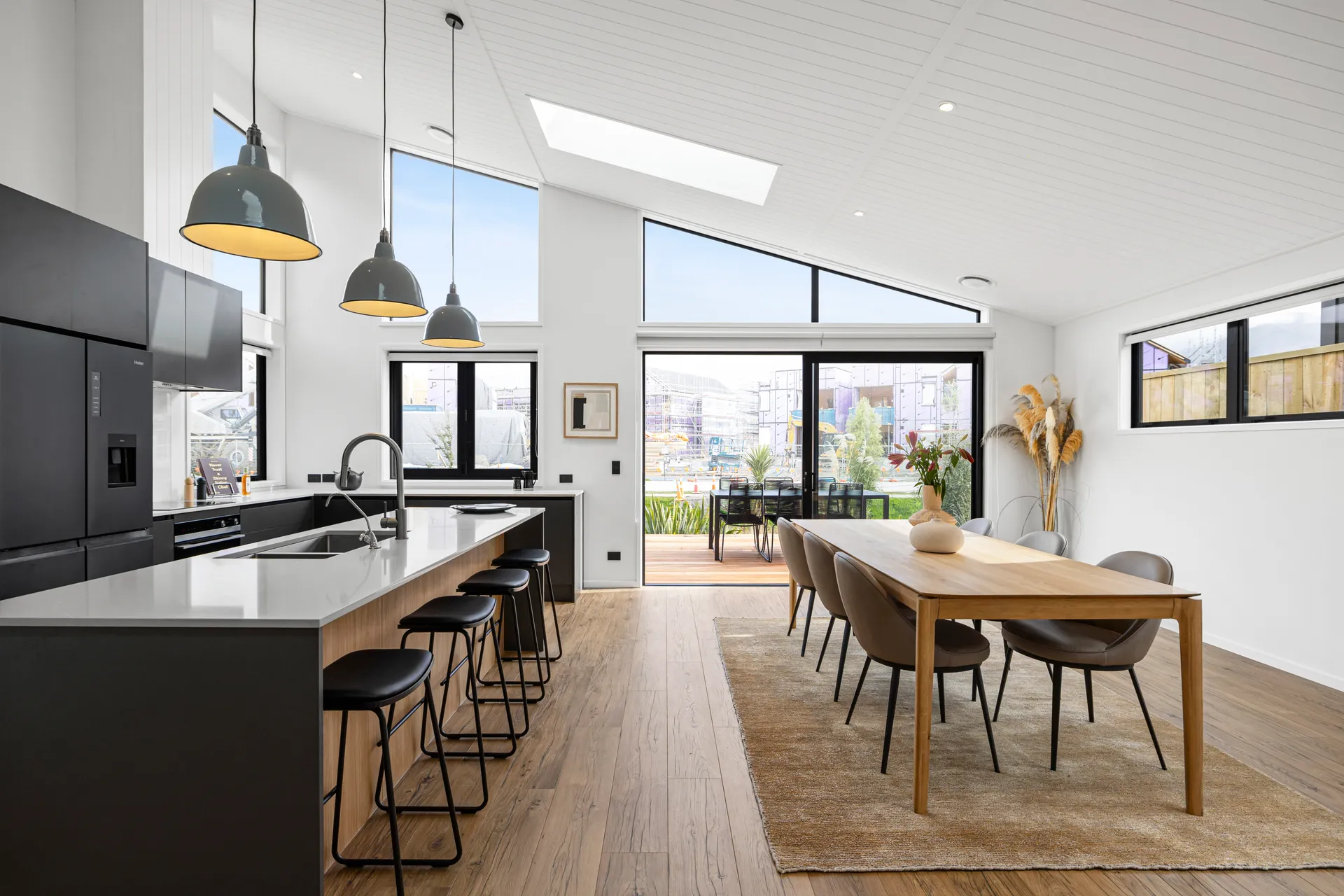 Long black kitchen run and island beside a dining table under a skylight