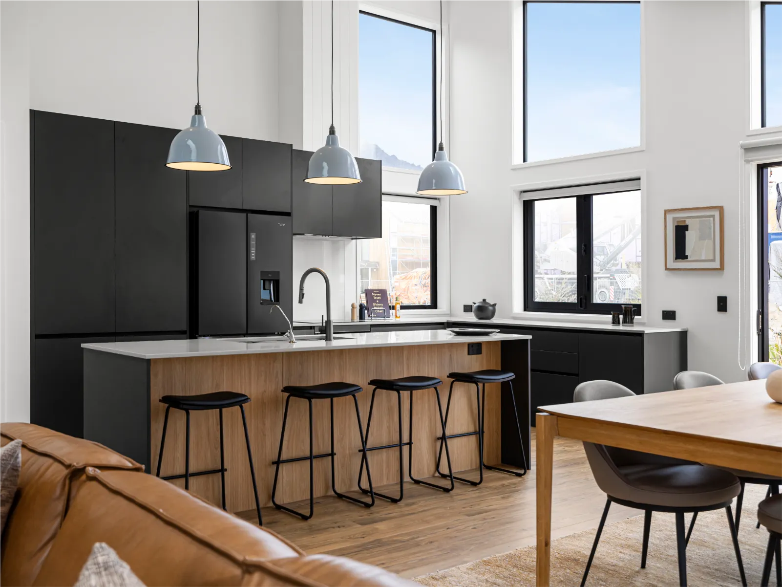 Timber-look island with black stools and black tall cabinets under high windows
