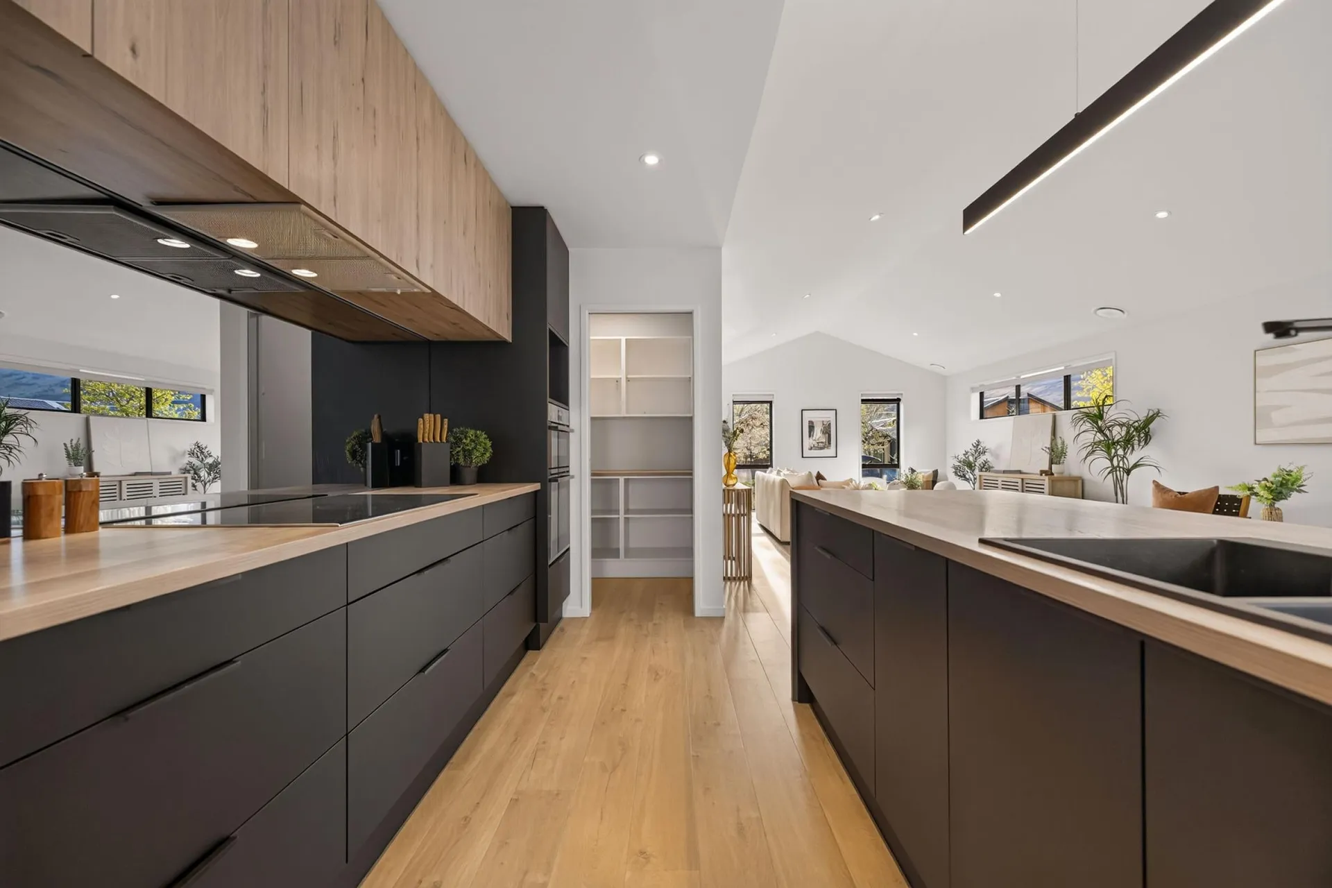 Black handleless galley with timber-look overheads and a walk-in scullery beyond