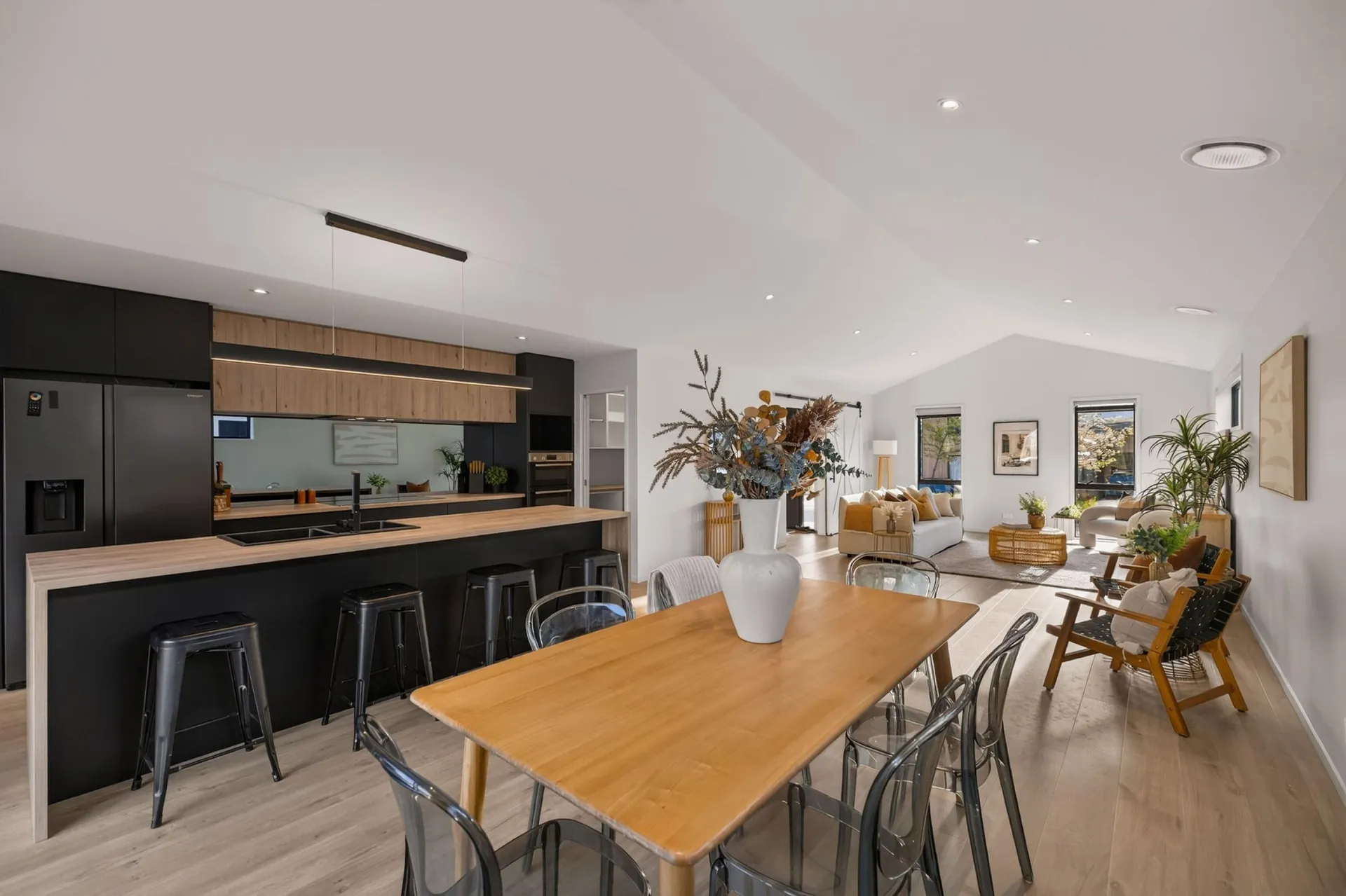 Full black kitchen run with timber-look overheads seen across the dining table