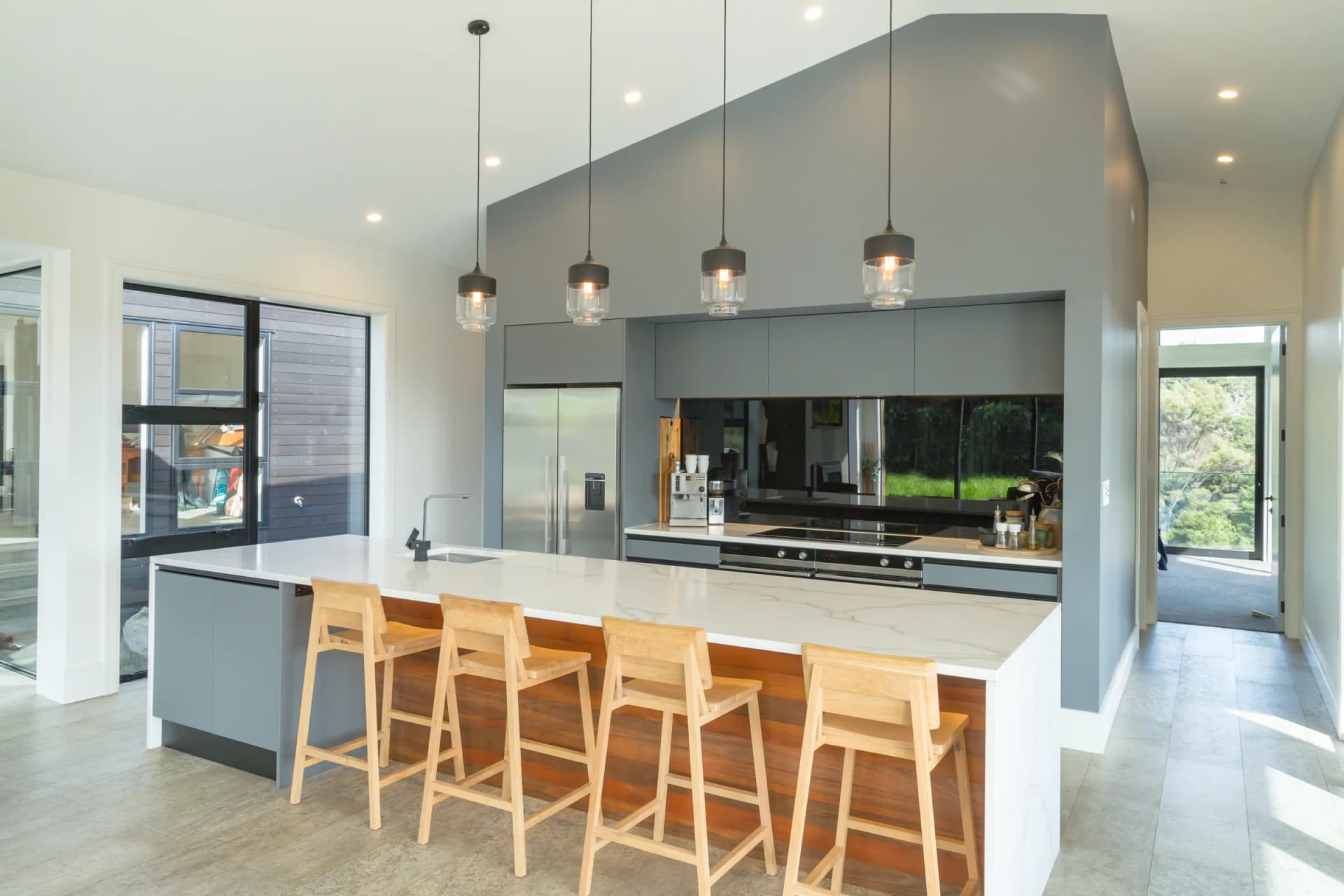 Grey handleless kitchen with a marble-look waterfall island and timber stools under a gable