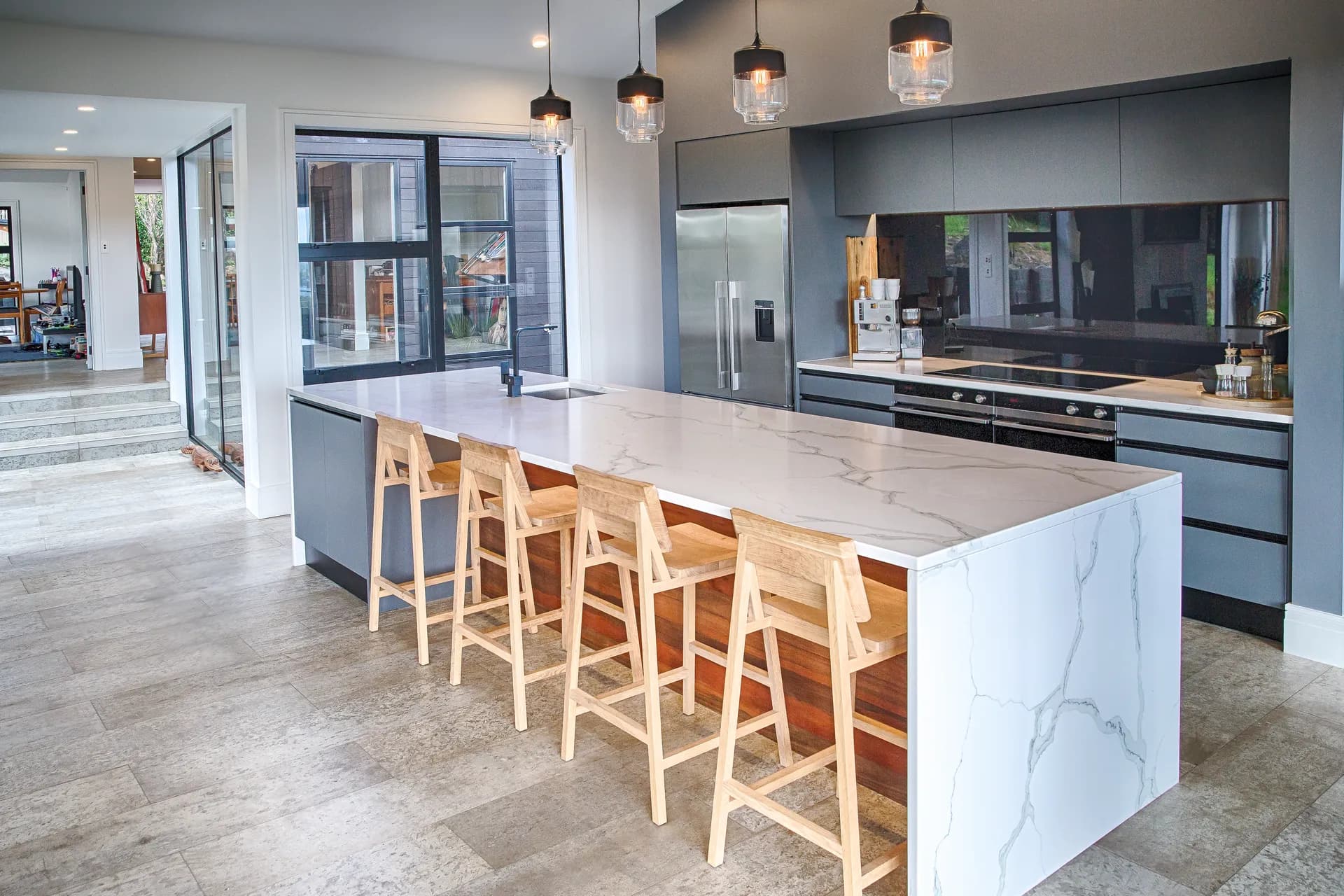 Long marble-look waterfall island with timber stools in front of grey cabinetry