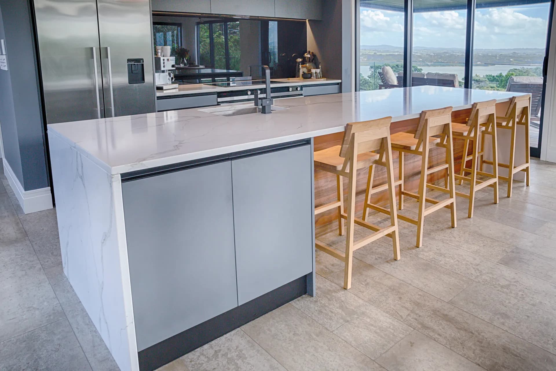 Waterfall island end with timber stools and a water view