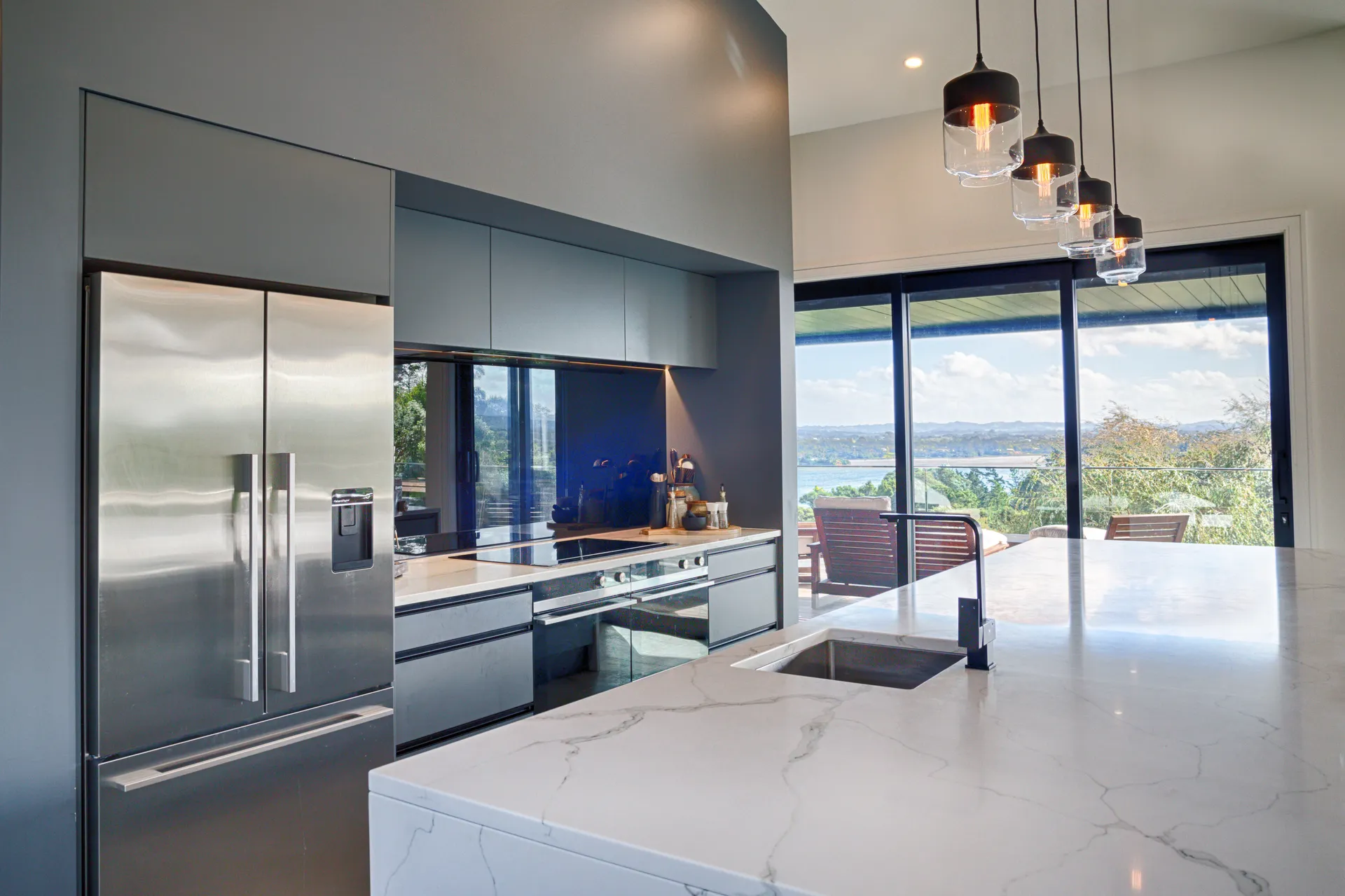 Grey cabinetry and island benchtop with pendant lights and a sea view