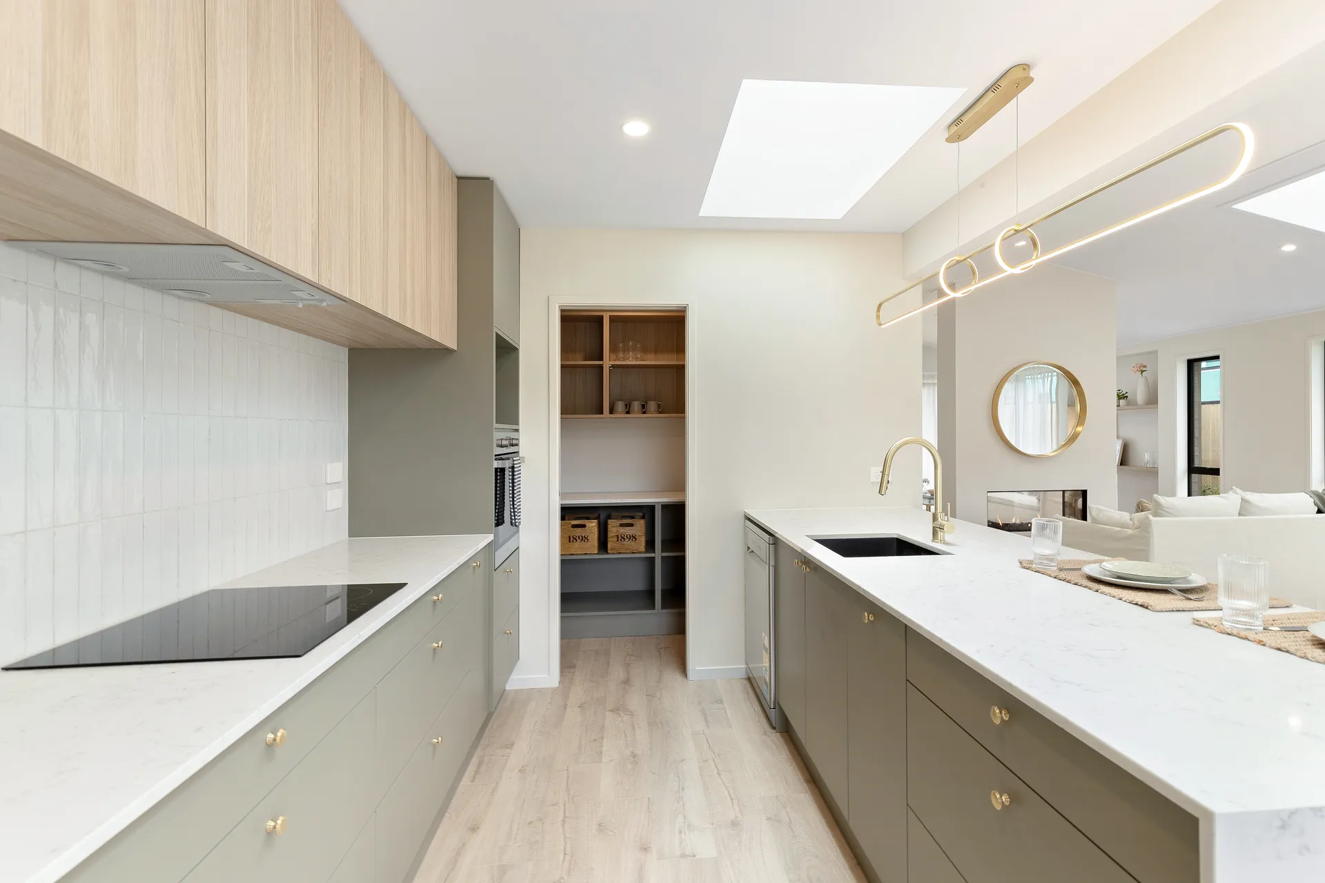 Galley between sage-green drawers and the island leading to a scullery with open shelving