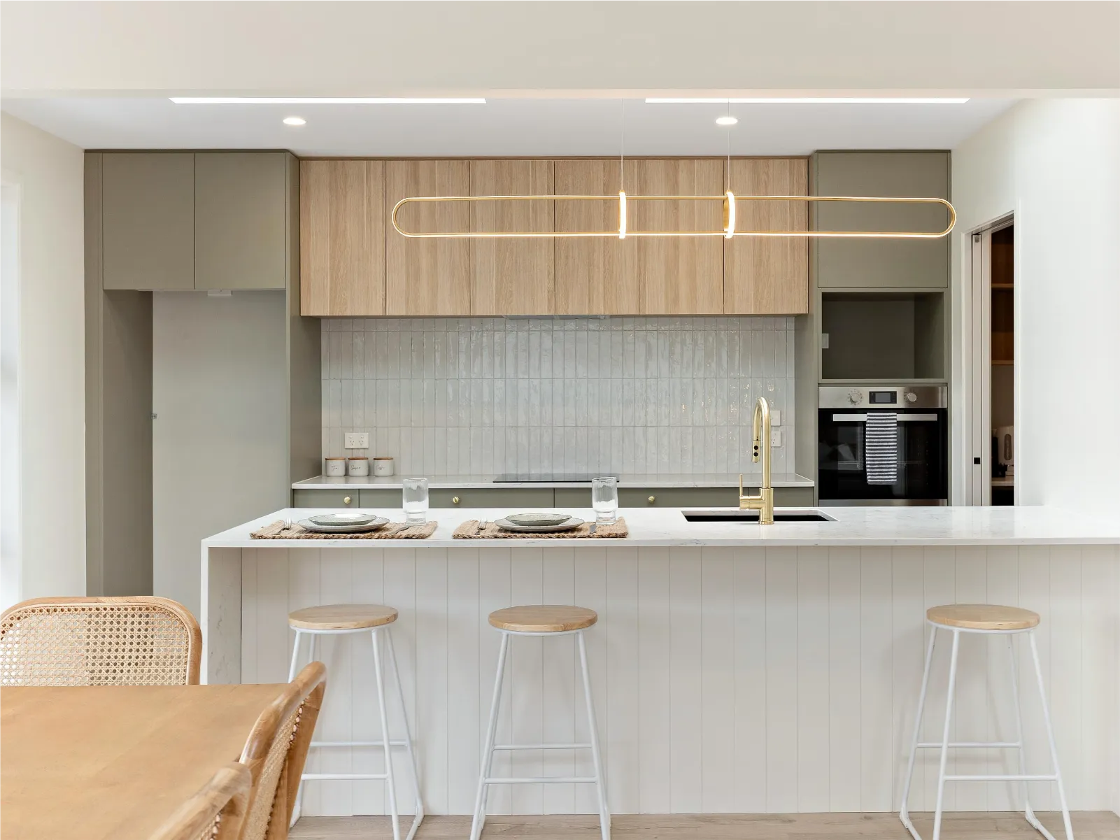 White panelled island with stools in front of sage and timber-look cabinetry