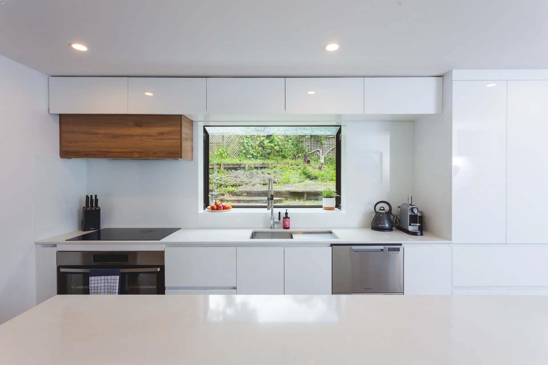 White gloss run with a window splashback and a timber-look box above the cooktop