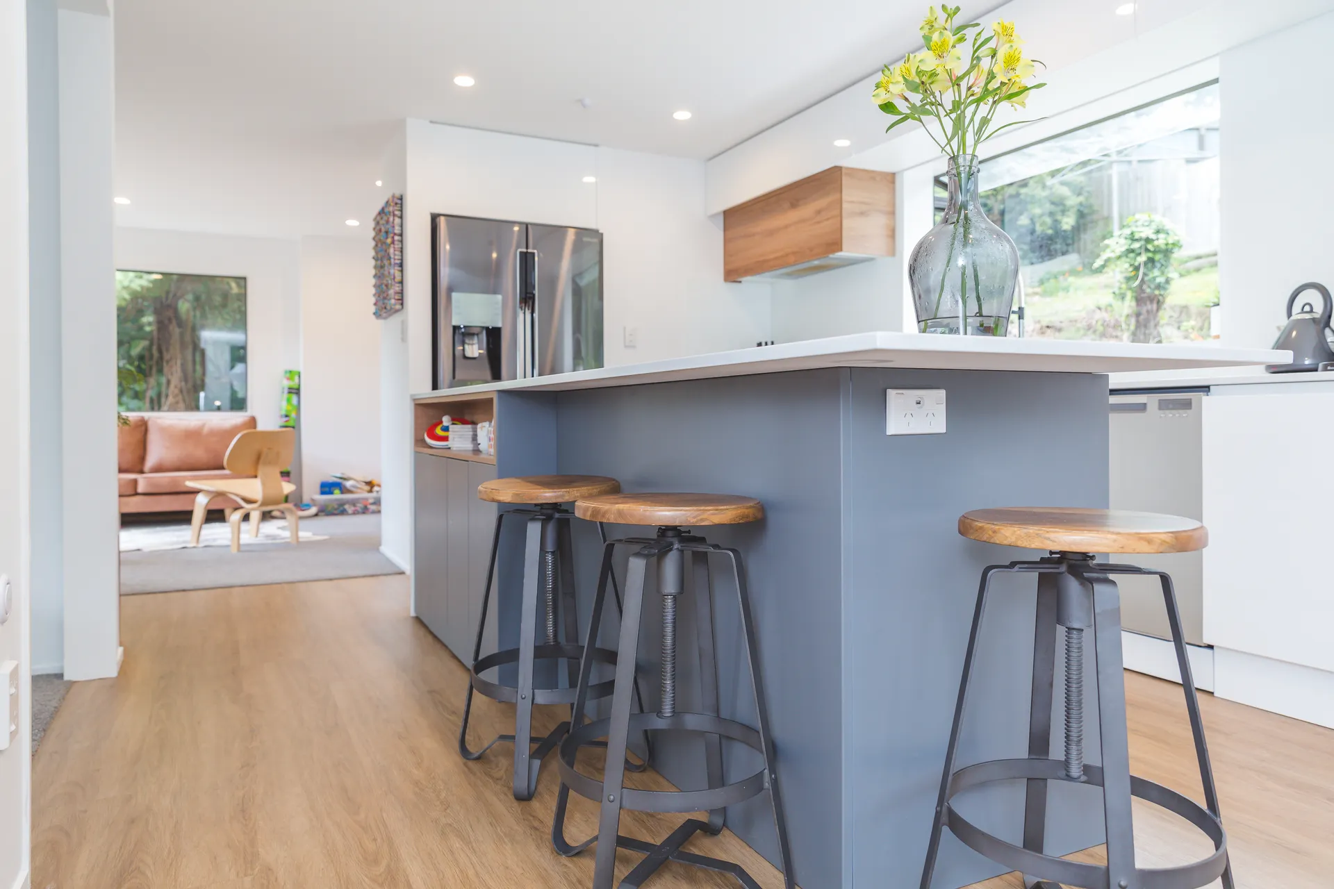 Grey island with stools in front of white gloss cabinets