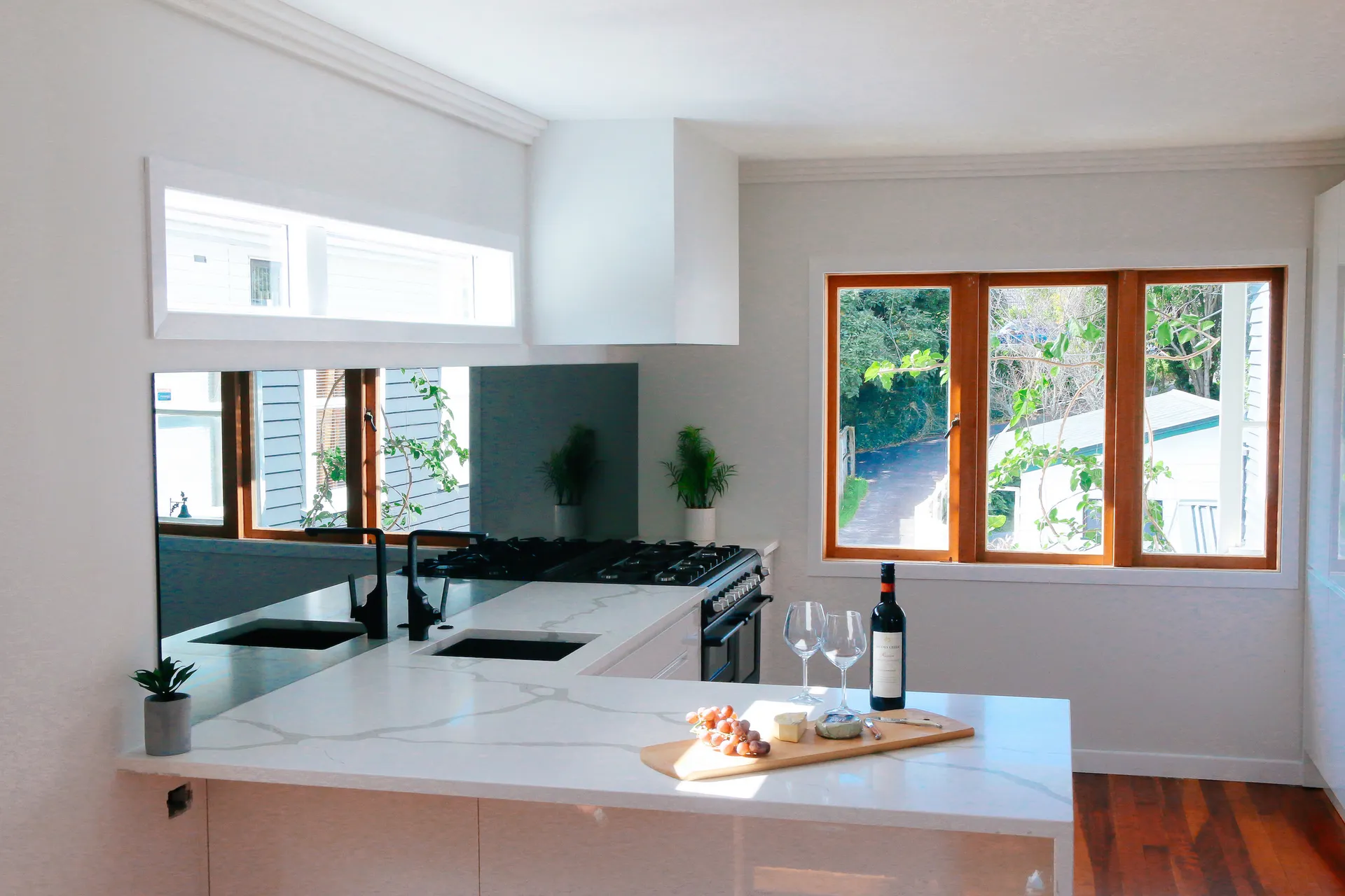 White peninsula with a marble-look benchtop below timber-framed windows