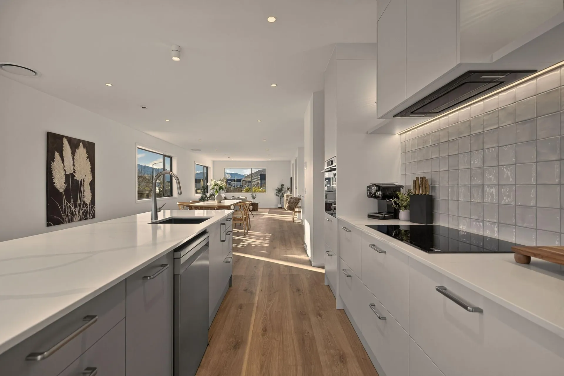 Galley view between the island and white cabinets with bar handles and a tiled splashback