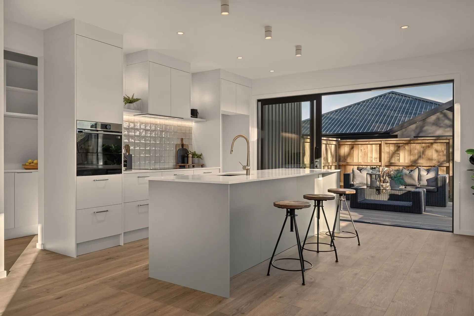 White kitchen and island with bar stools opening onto an outdoor living area