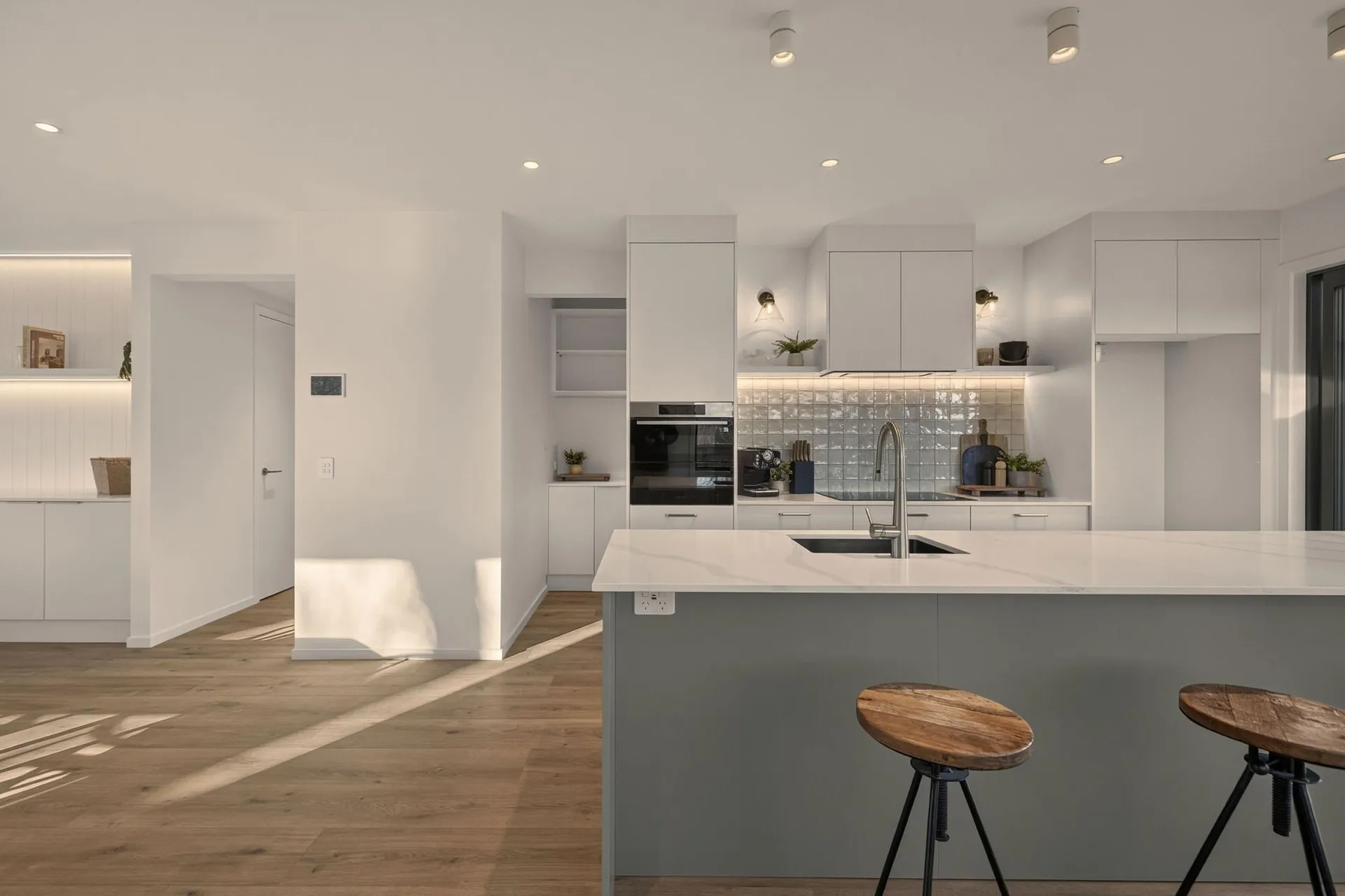 Wide view of the grey-green island, white cabinetry and tiled splashback