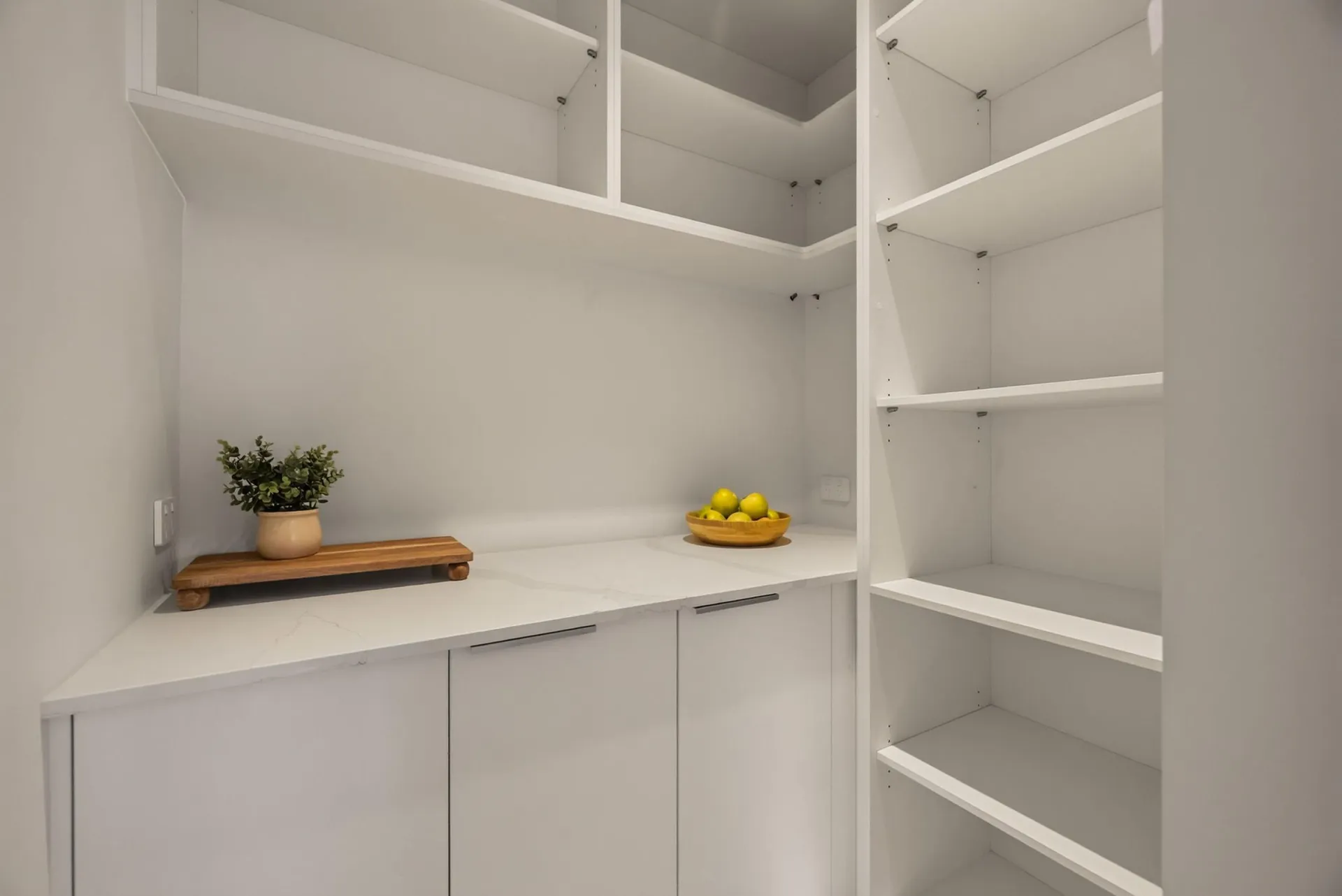 White scullery with open corner shelving and a bench above cupboards