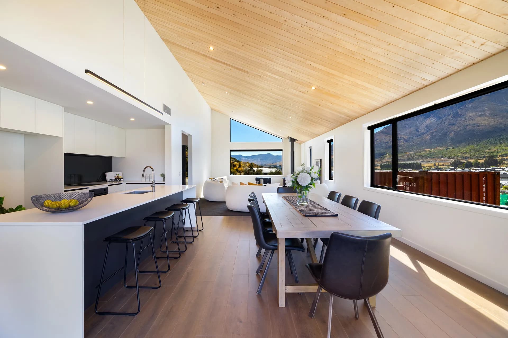 Dark island with stools beside a long dining table and a mountain view window