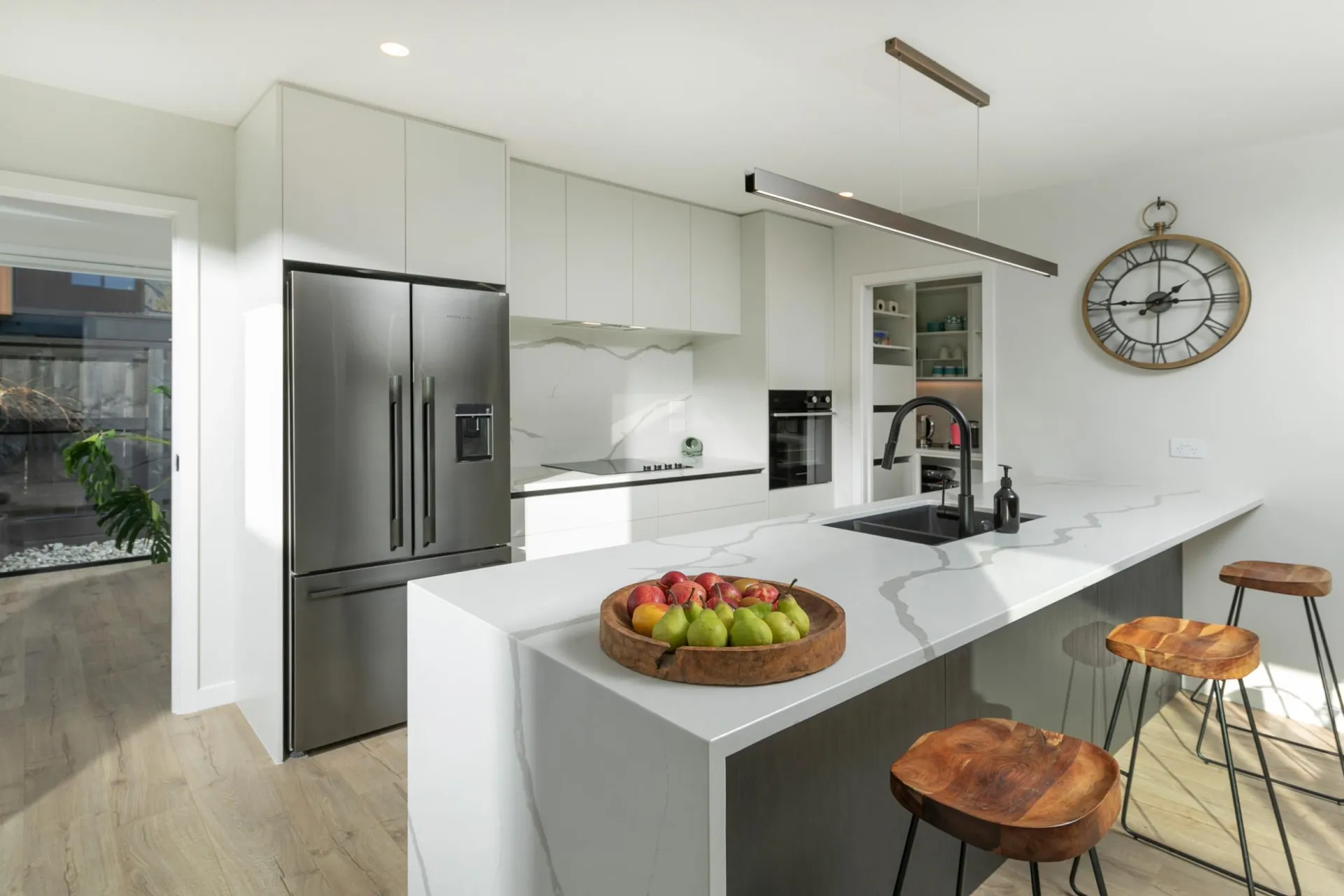 Marble-look waterfall island with timber stools and white tall cabinets with a wall oven