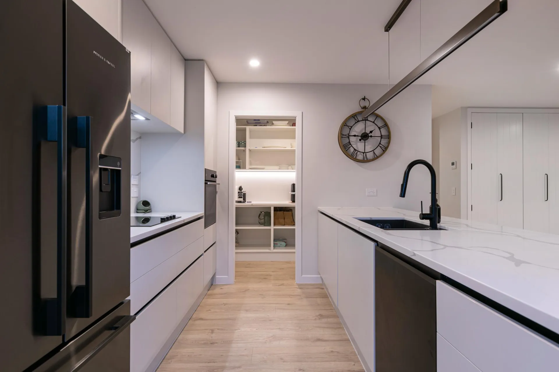 Galley run with handleless white drawers and a walk-in scullery with lit shelving beyond