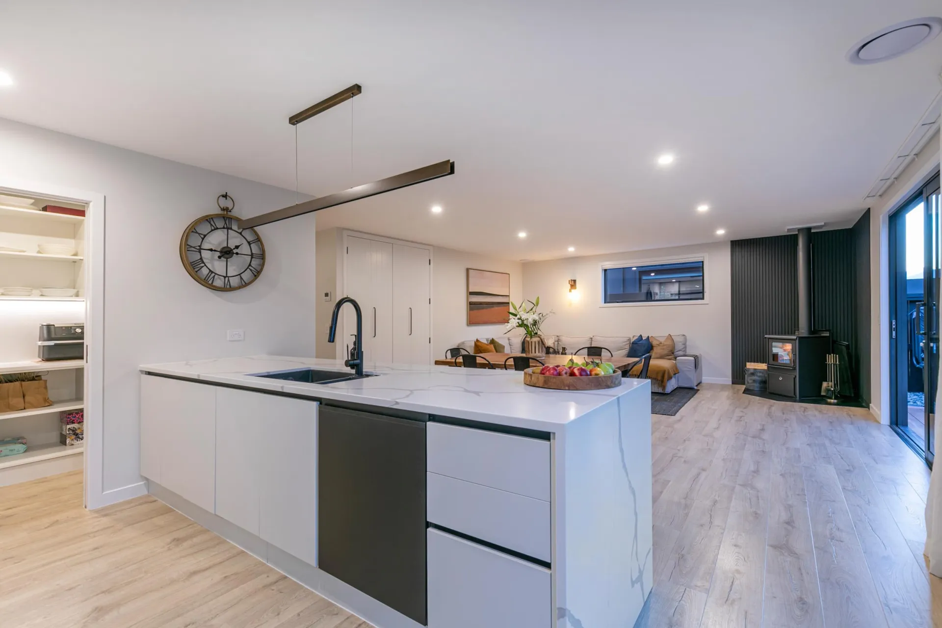 White and dark island from the living end with open pantry shelving at left