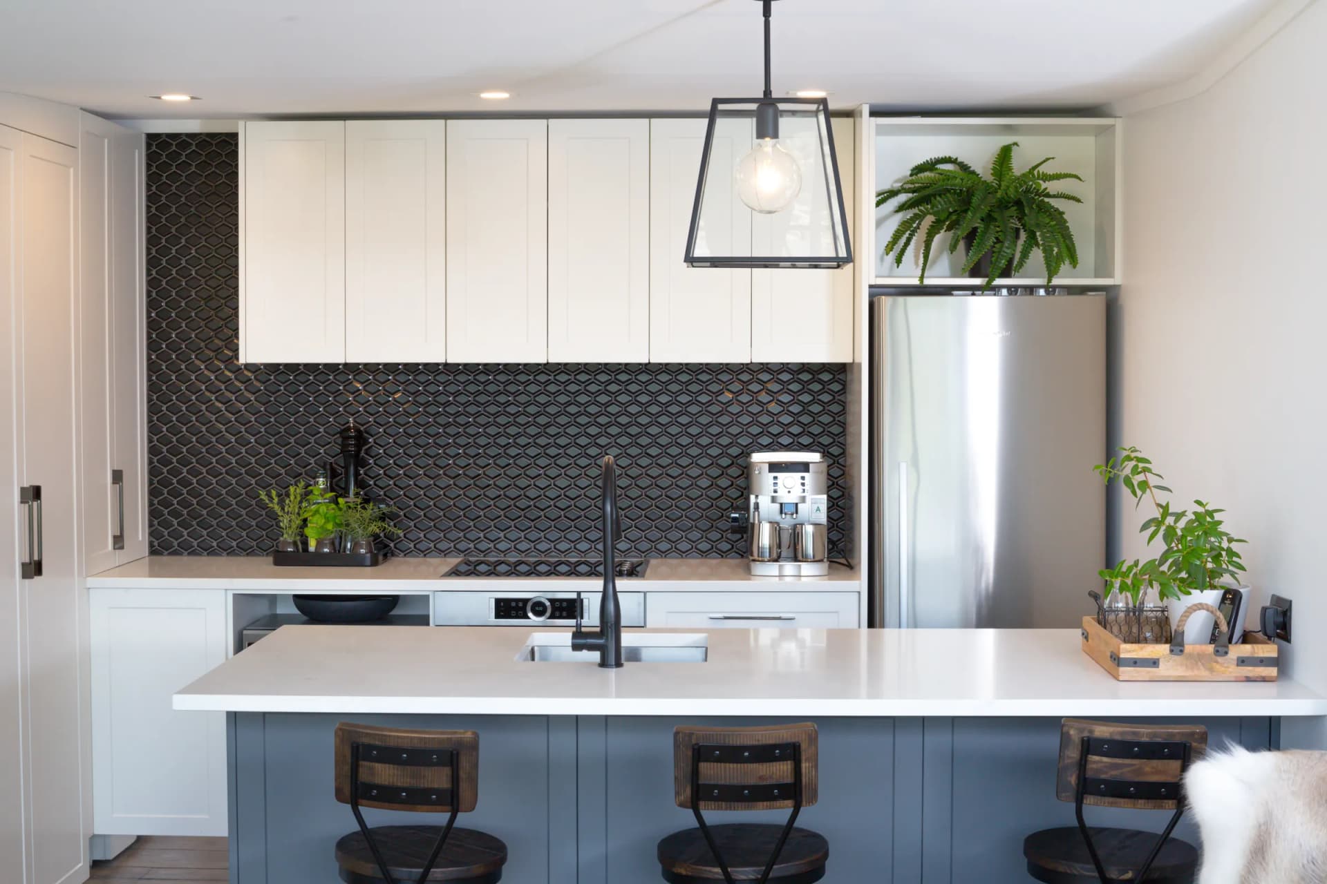 Blue-grey island with stools in front of white overheads and a dark patterned tile splashback