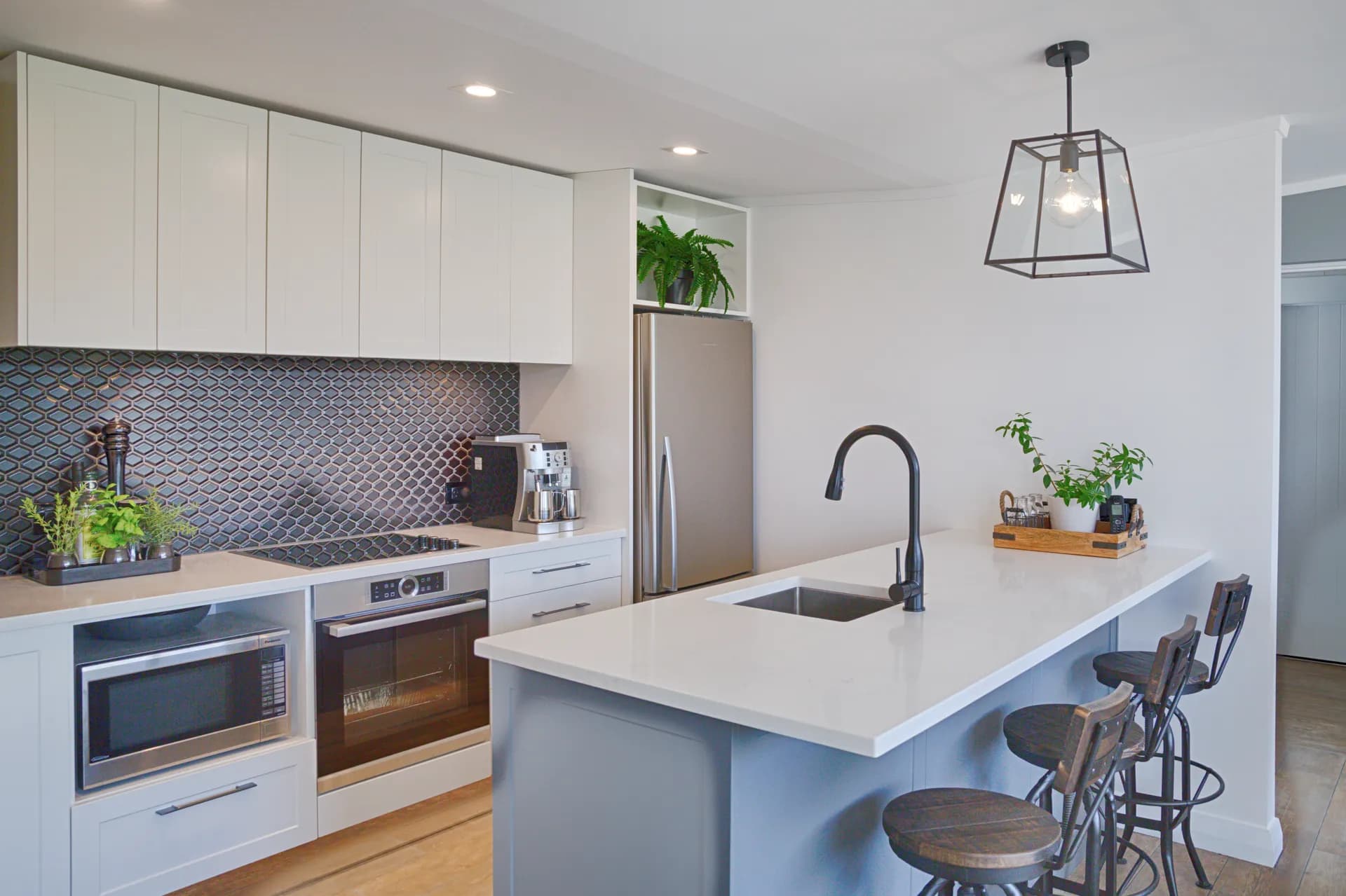 White overheads, dark patterned tiles and a blue-grey island with stools