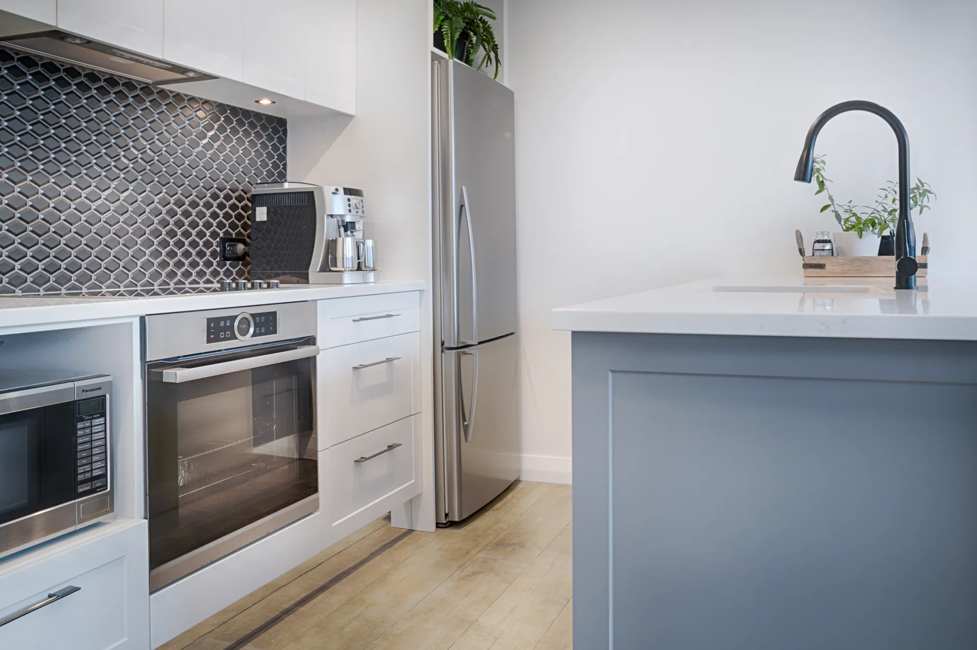 Oven and microwave run beside the island end and a patterned tile splashback