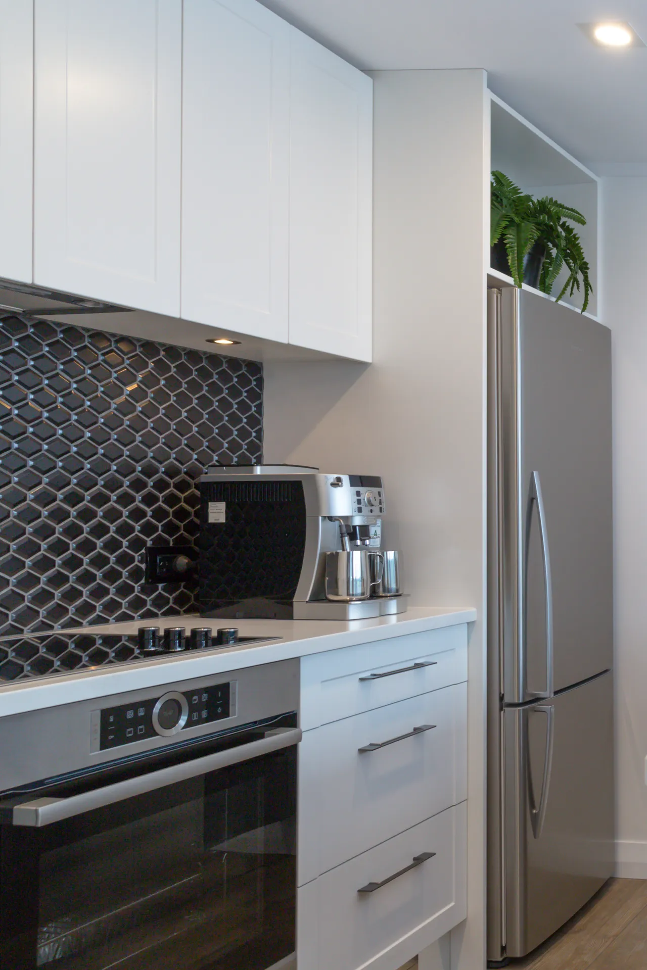 White overheads and drawers with bar handles beside a fridge nook