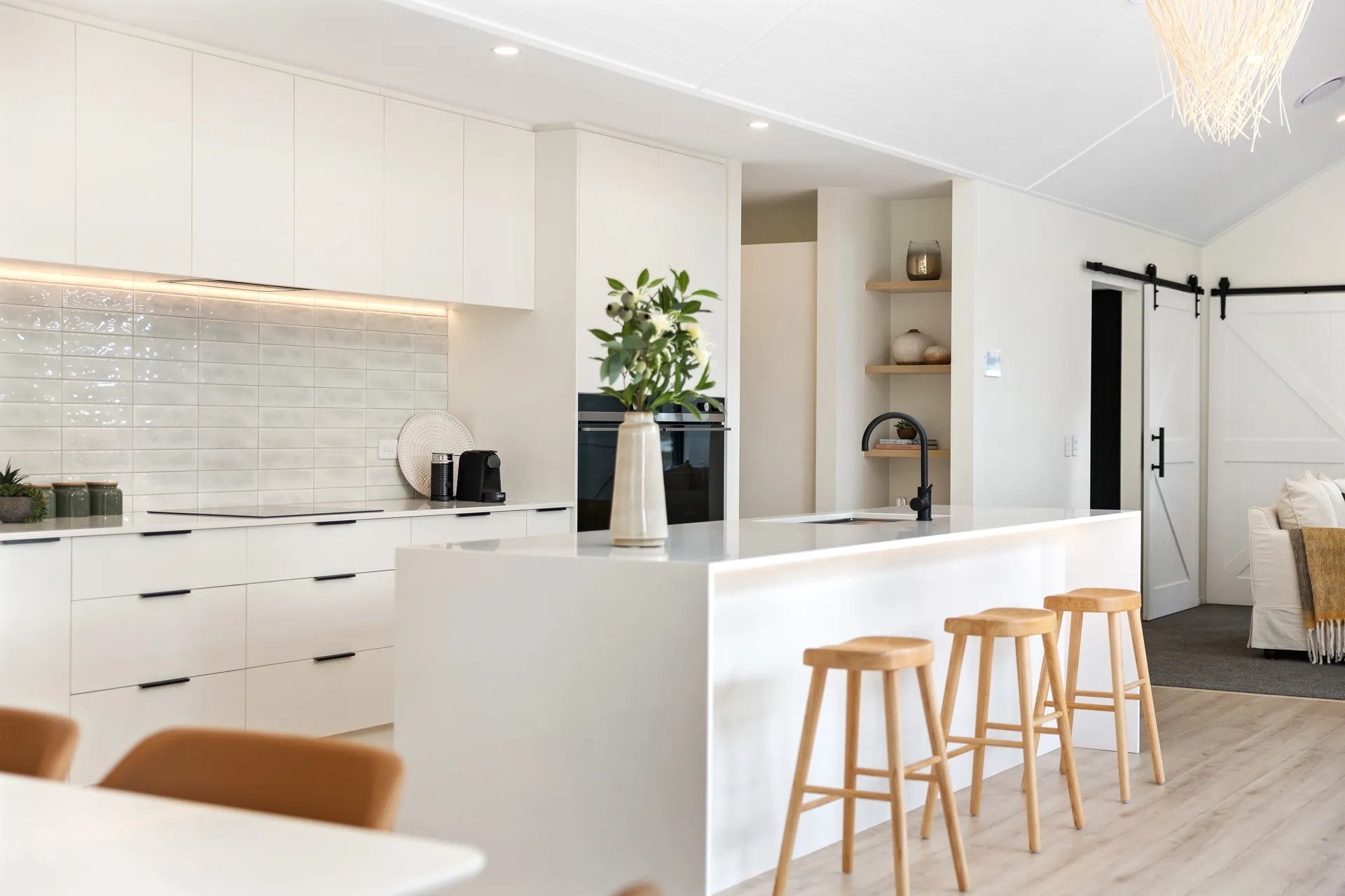 White island with timber stools and white cabinets with black bar handles under a raked ceiling