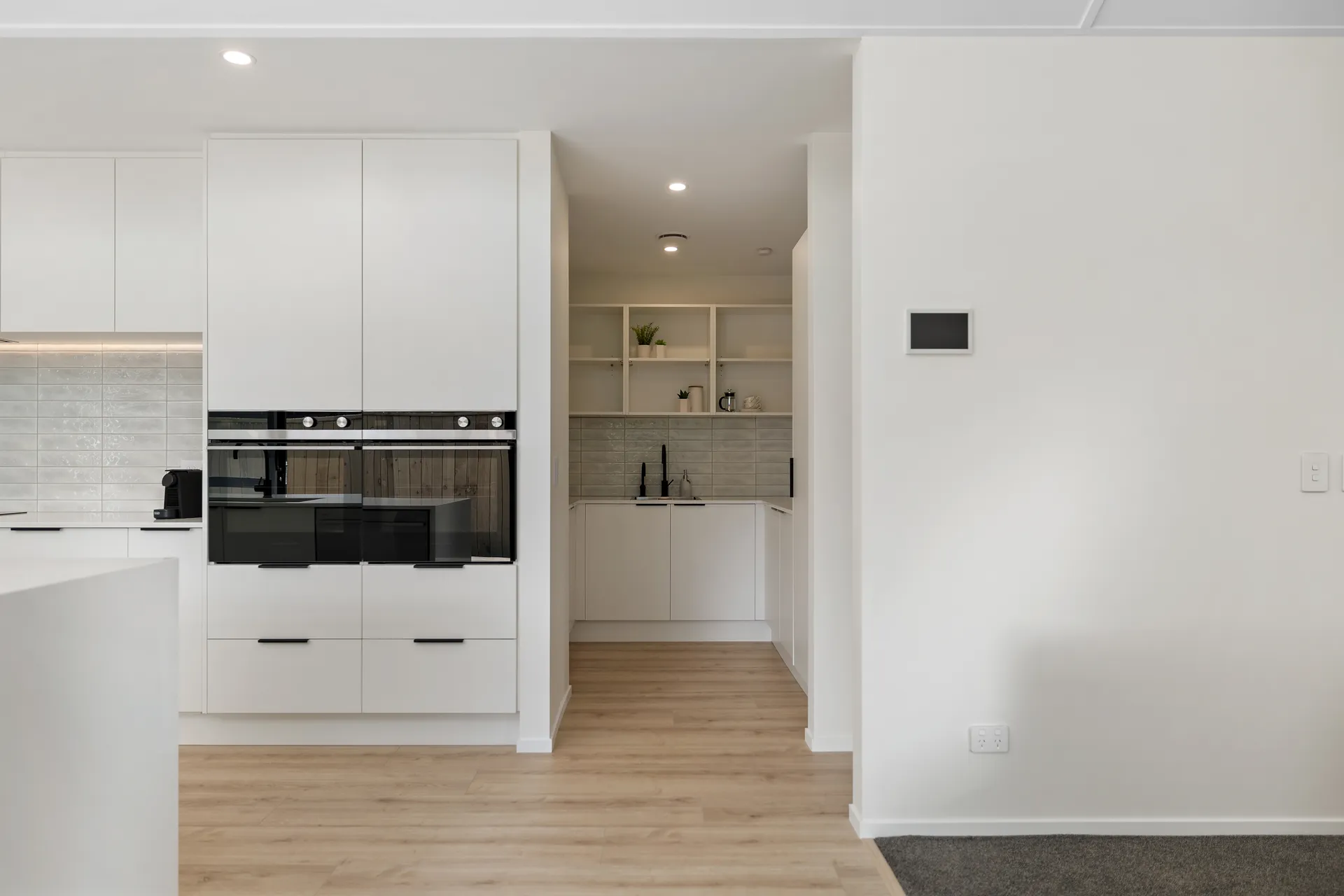 Tall white cabinets with wall ovens and a scullery with open shelving beyond