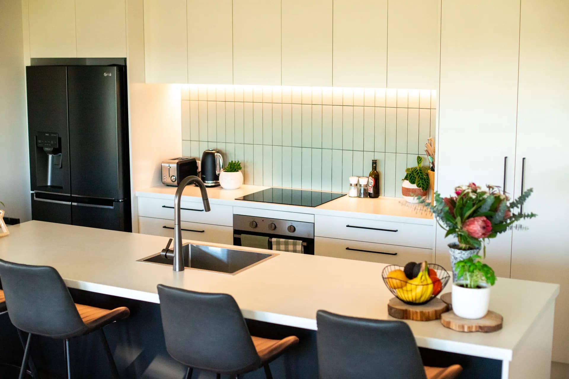 Navy island and bar stools in front of white cabinets and a lit tiled splashback