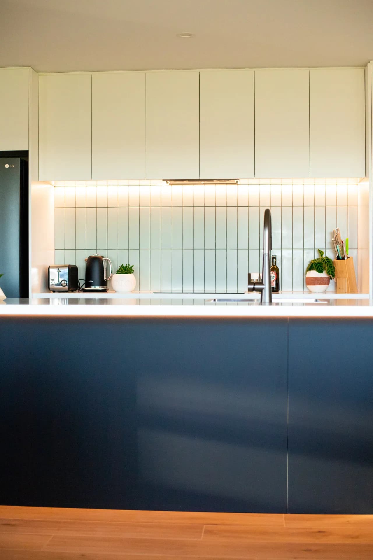 Front-on navy island below white overheads and a lit tiled splashback