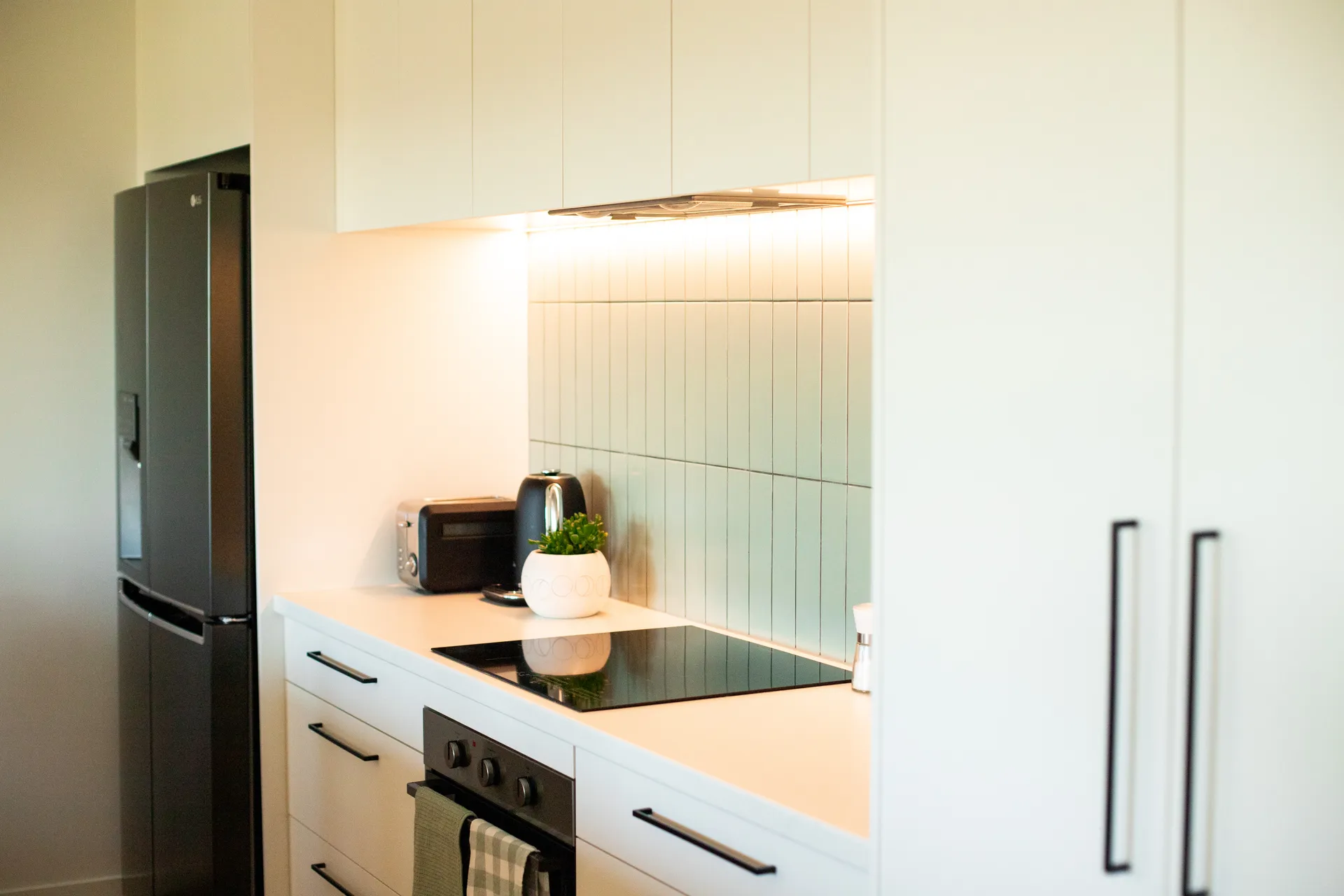 Cooktop run with a tiled splashback beside tall white doors with black handles