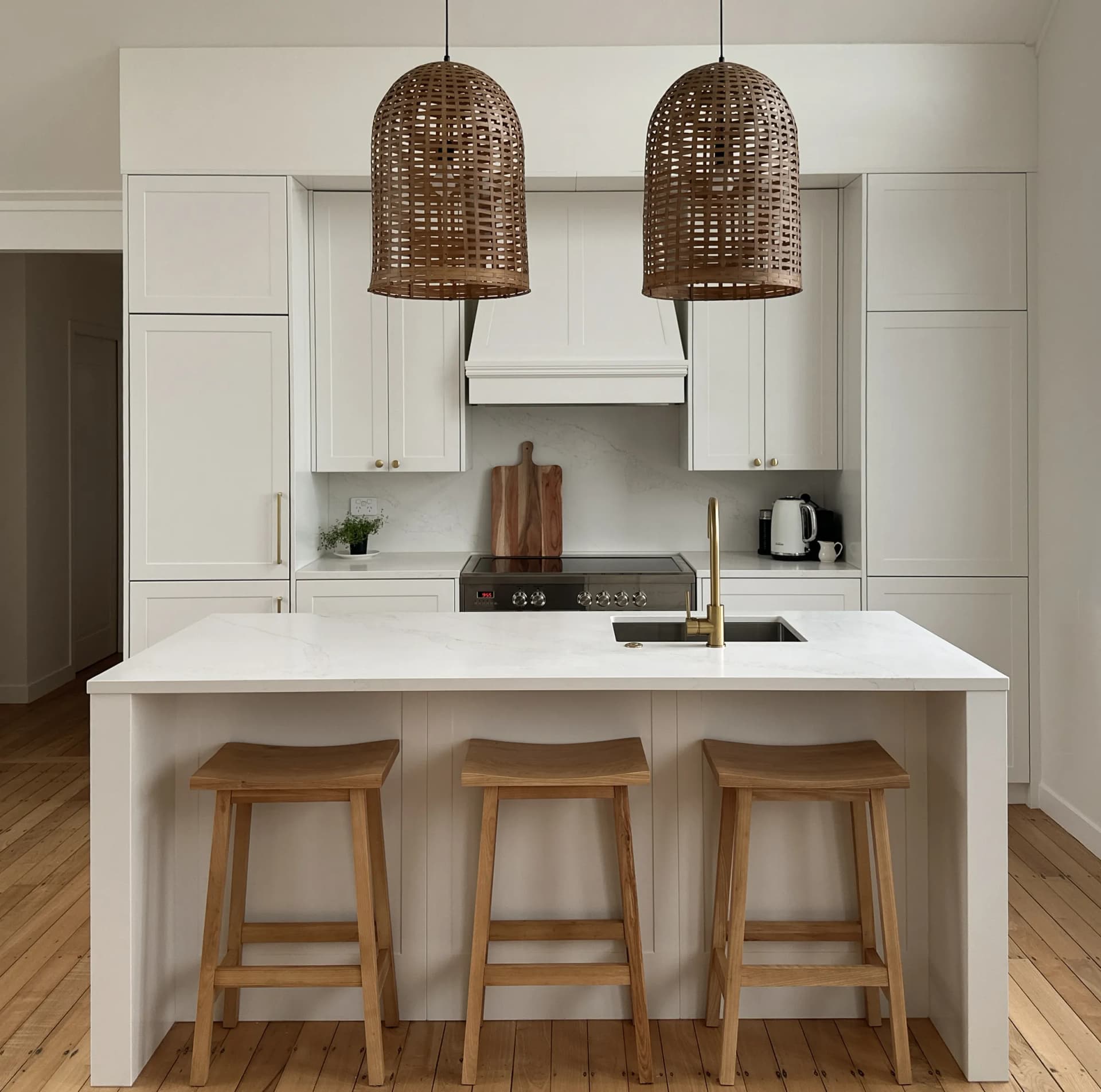 White shaker kitchen with a canopy rangehood, woven pendants and timber stools at the island