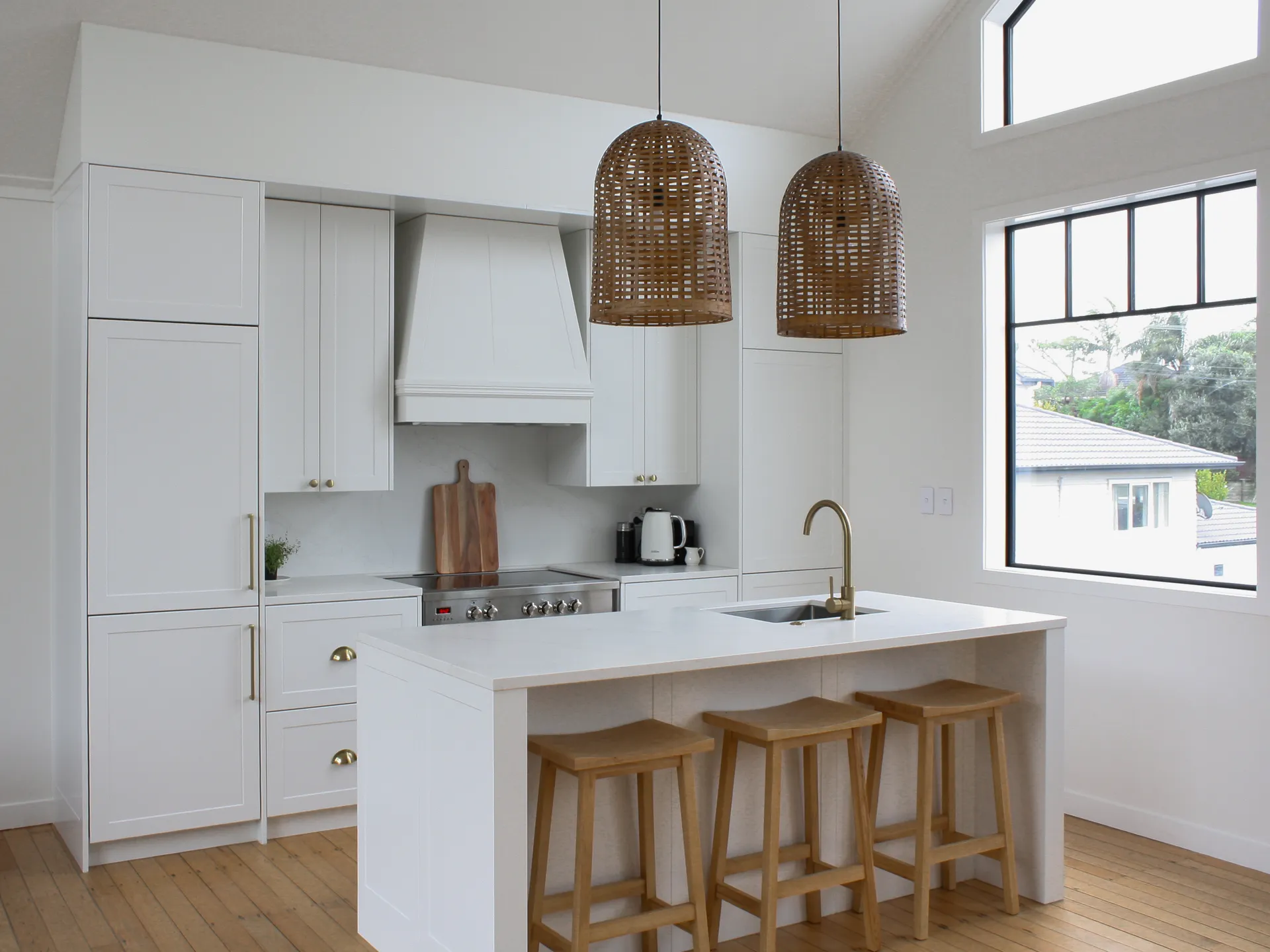 White shaker kitchen with an island and timber stools beside tall black-framed windows