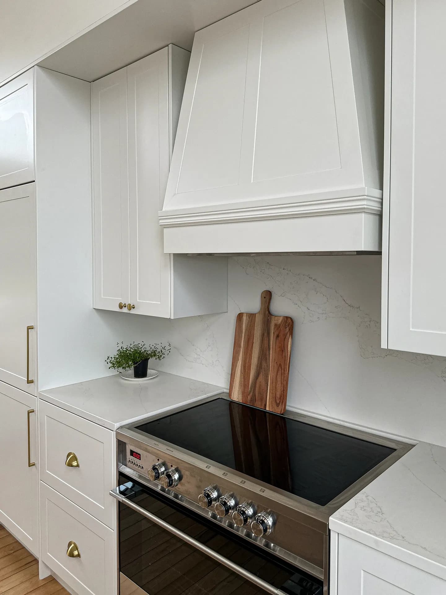 Canopy rangehood over a freestanding cooker between white shaker cabinets