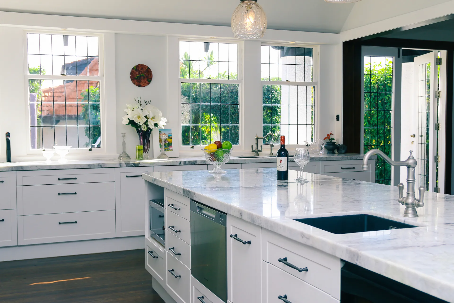 White shaker cabinets and island sink in front of leadlight windows