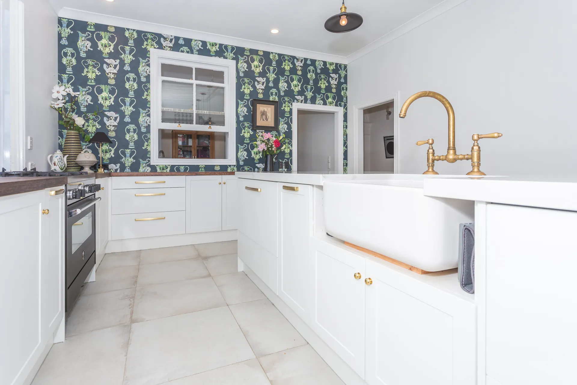 Butler sink in a white shaker run toward the wallpapered wall