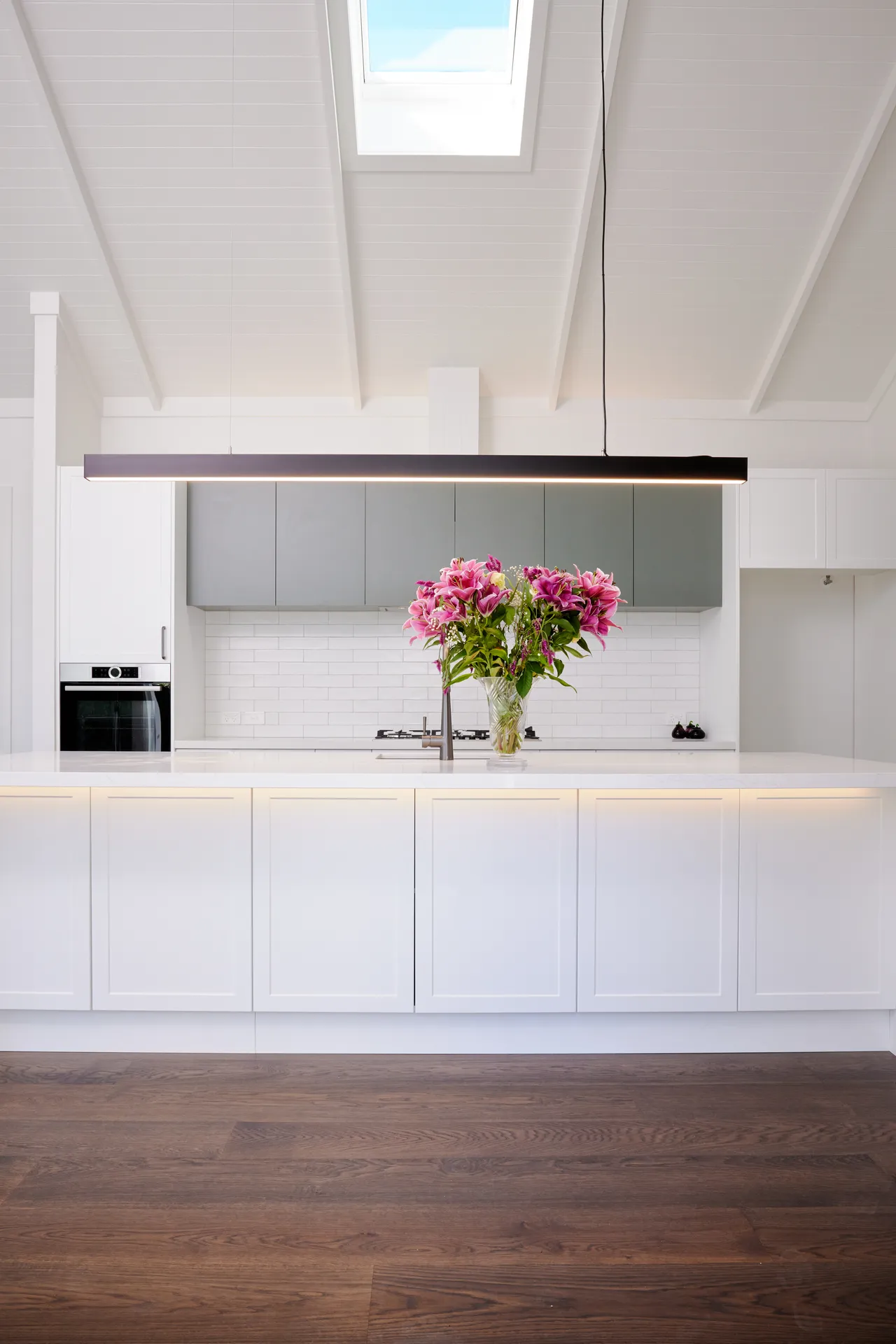 Symmetrical view of a white shaker island and sage overheads under a raked ceiling