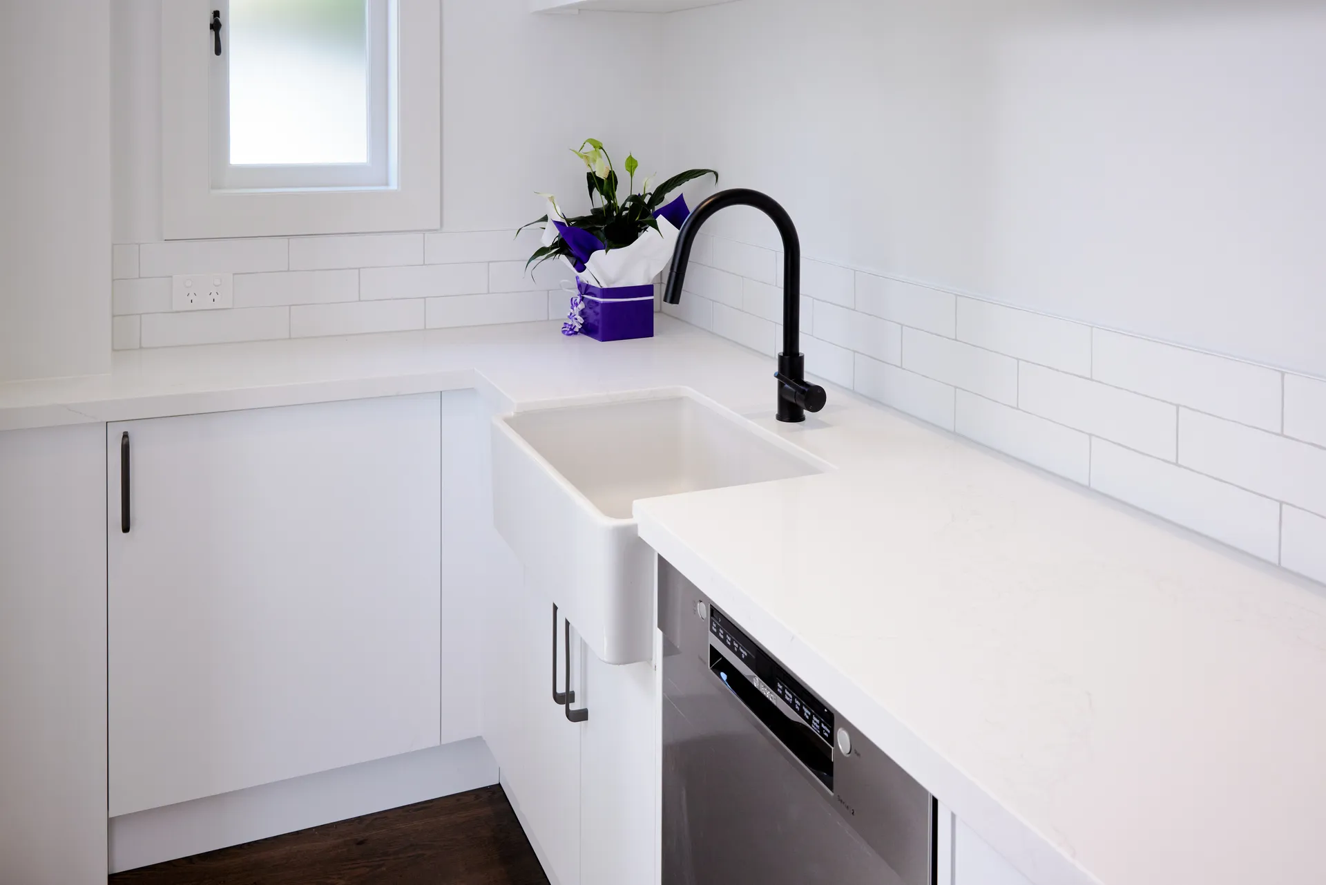 Butler sink set into white cabinets with black handles and a tiled splashback