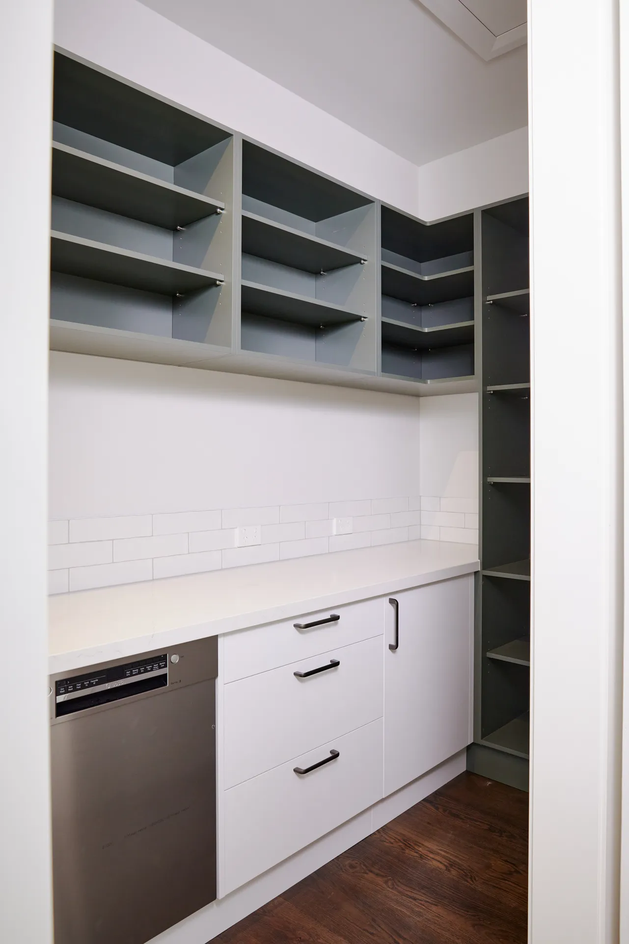 Scullery with sage open shelving above white drawers and a dishwasher