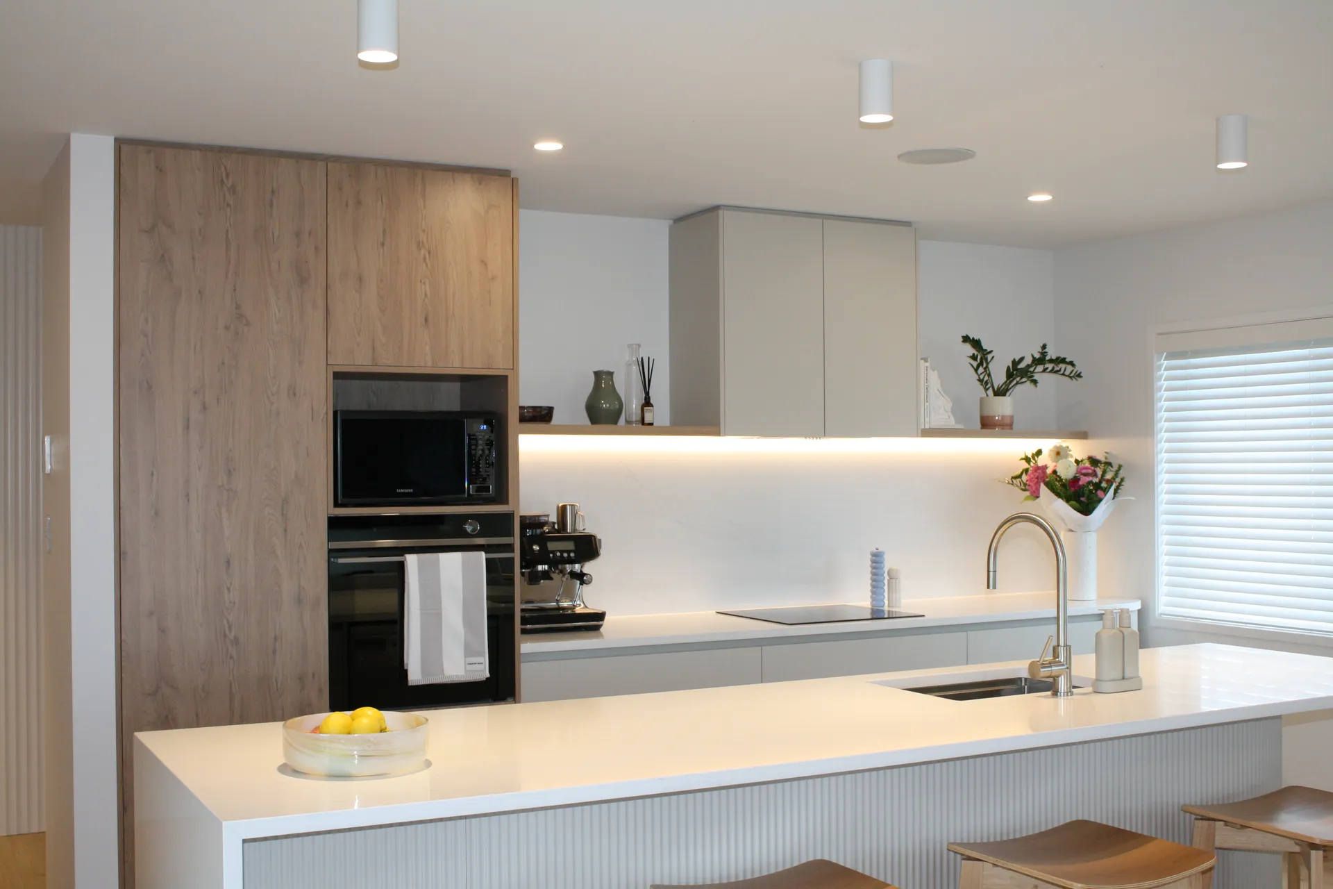 Timber-look tall cabinets with wall ovens and a lit shelf above the white benchtop