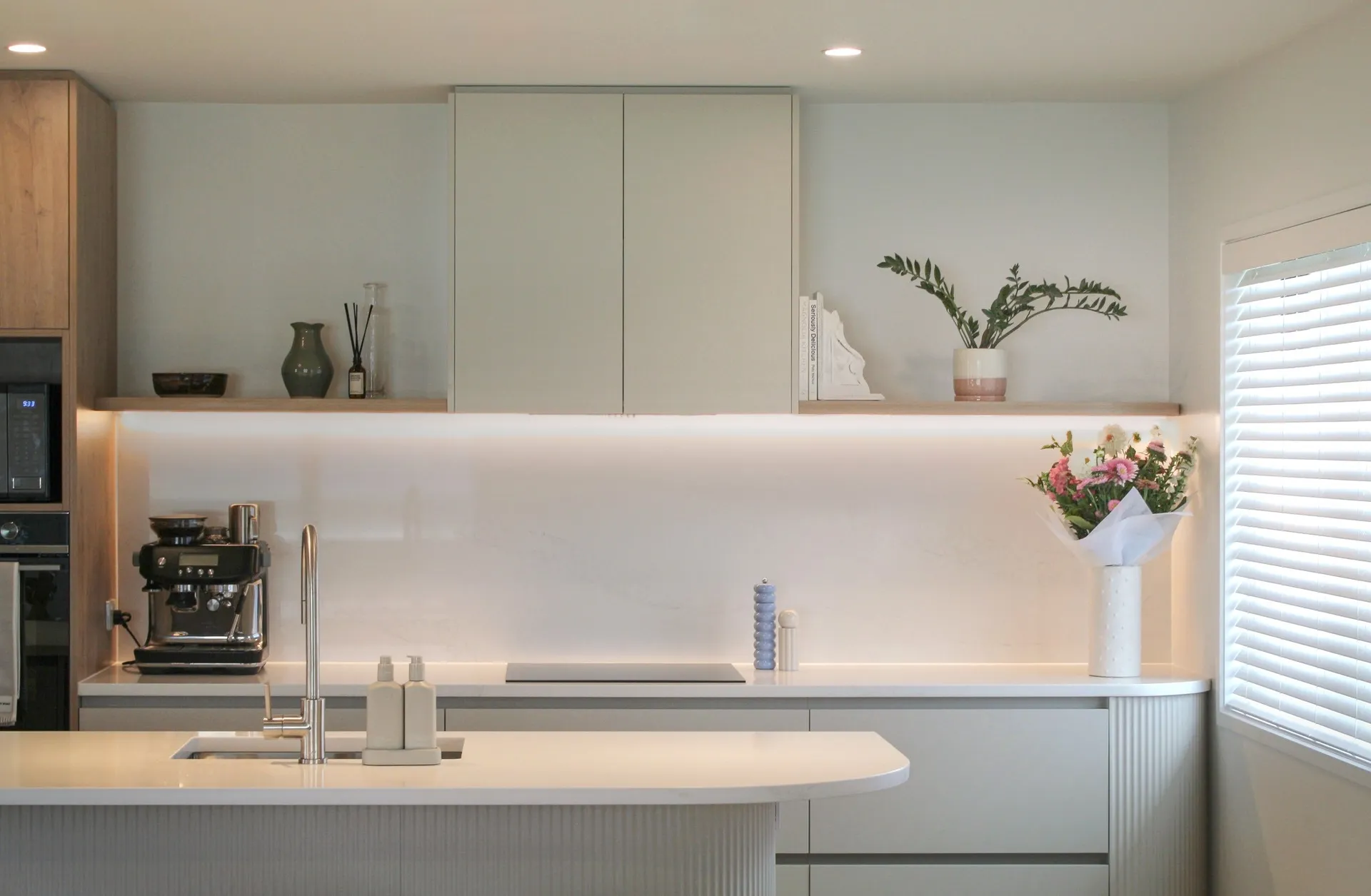 White back run with floating shelves and LED strip lighting behind a curved island