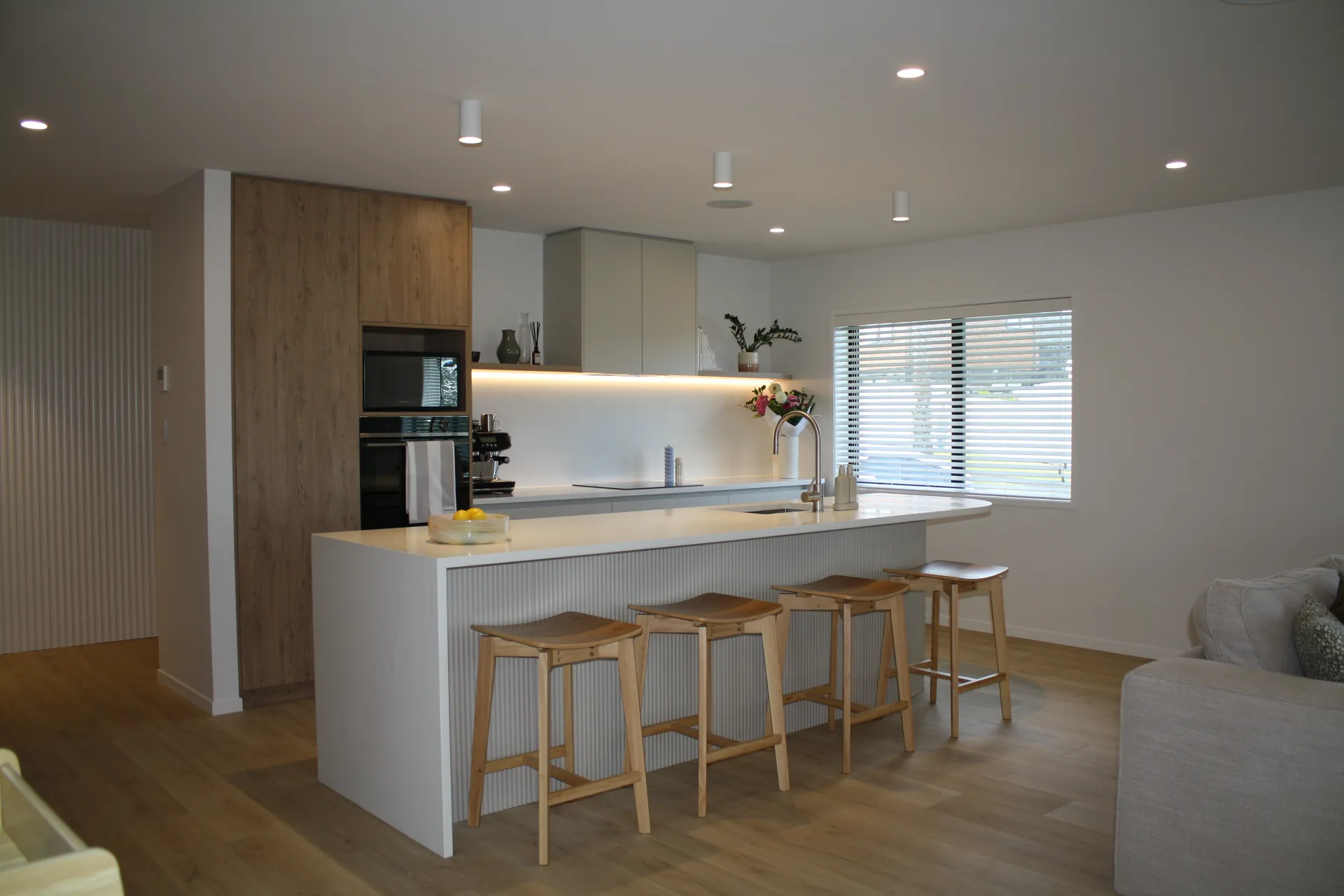 Three-quarter view of the fluted island with timber stools and timber-look tall cabinets