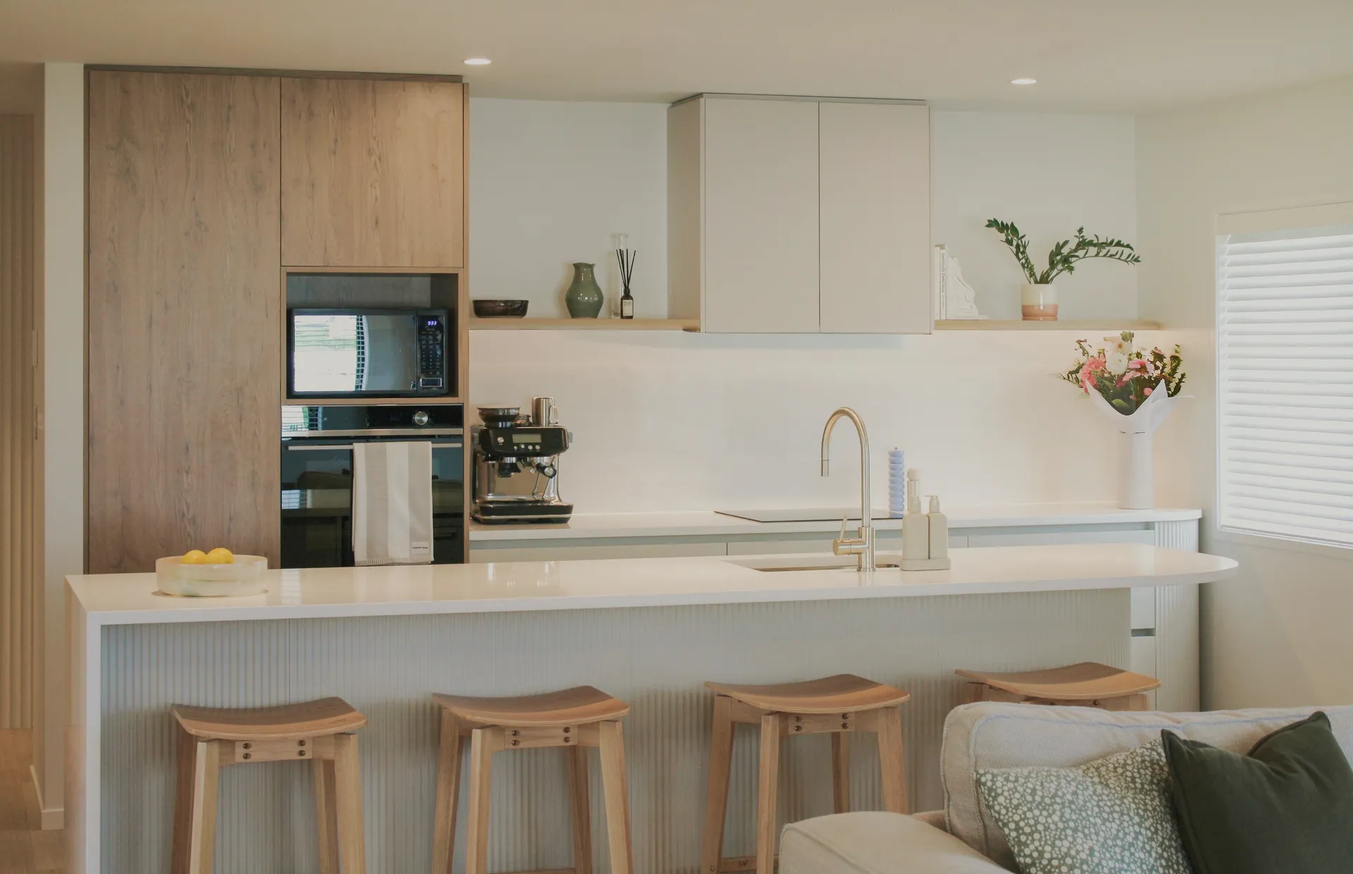 Fluted island breakfast bar with timber stools facing a white and timber-look kitchen