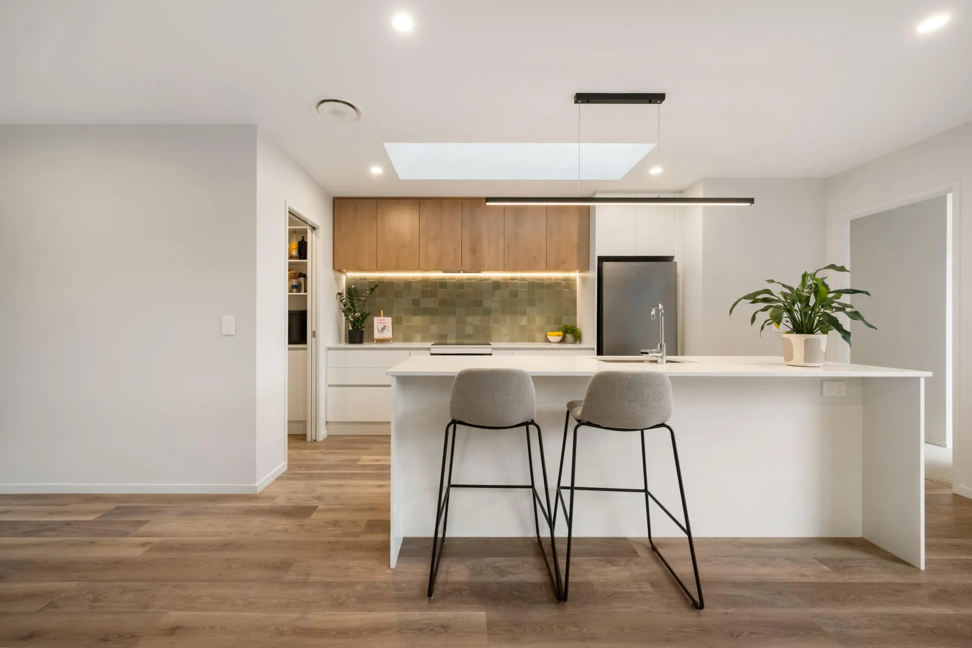 Front-on white island with bar stools, timber-look overheads and a skylight above