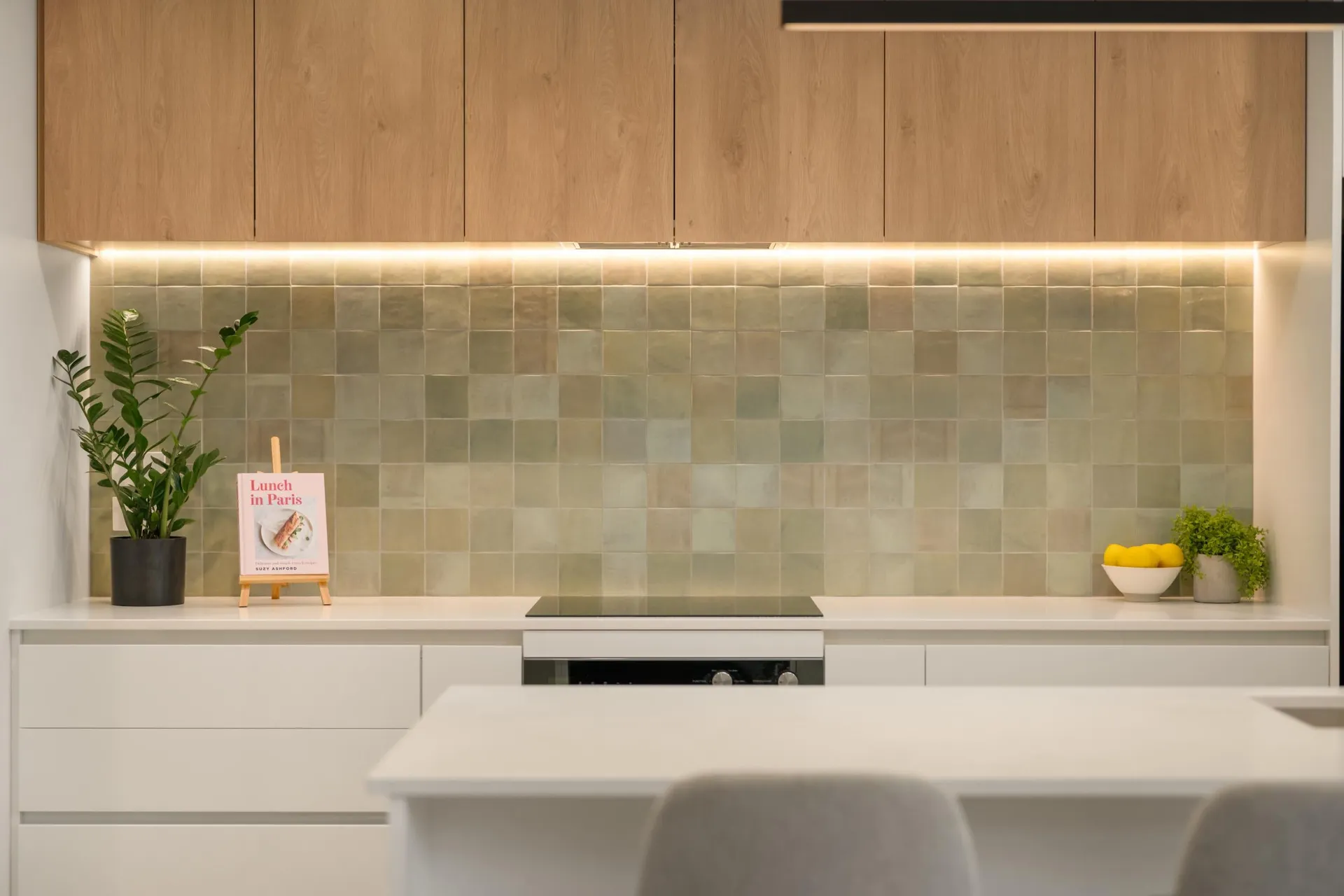 Timber-look overheads with LED strip lighting above a green tiled splashback and white drawers