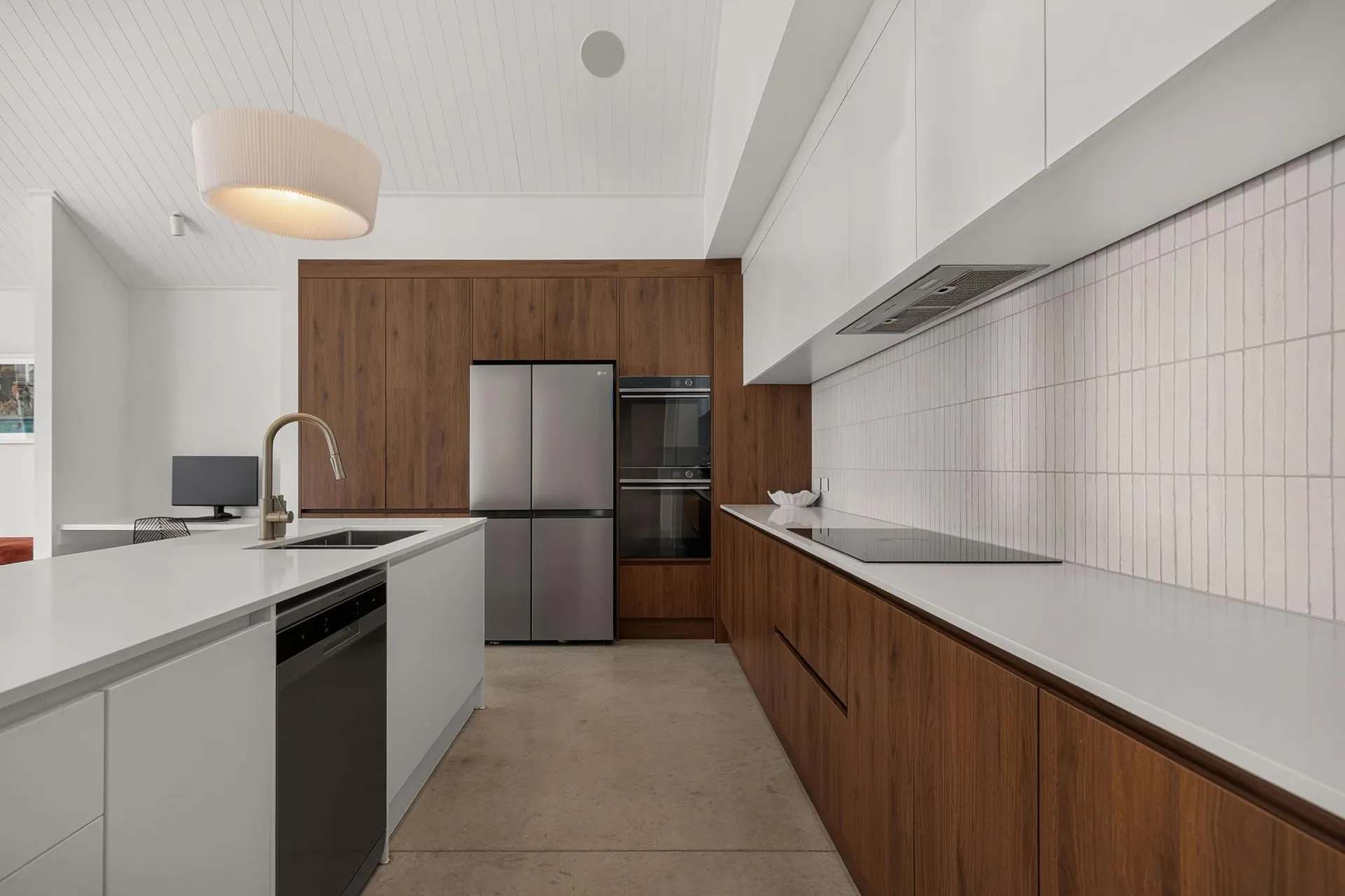 Galley between a white island and timber-look base cabinets under white handleless overheads