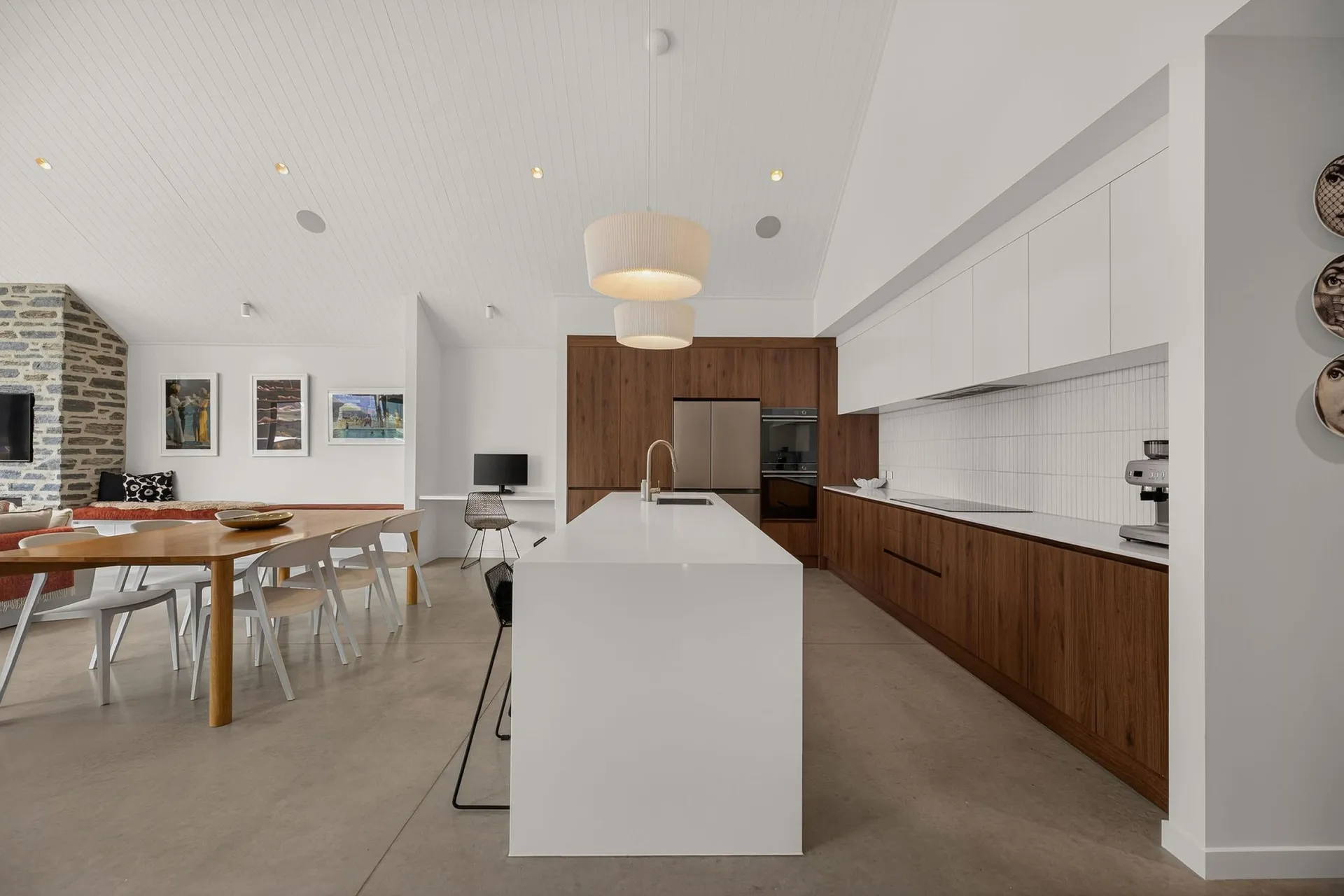 Long white island and timber-look cabinetry under a vaulted ceiling with pendant lights