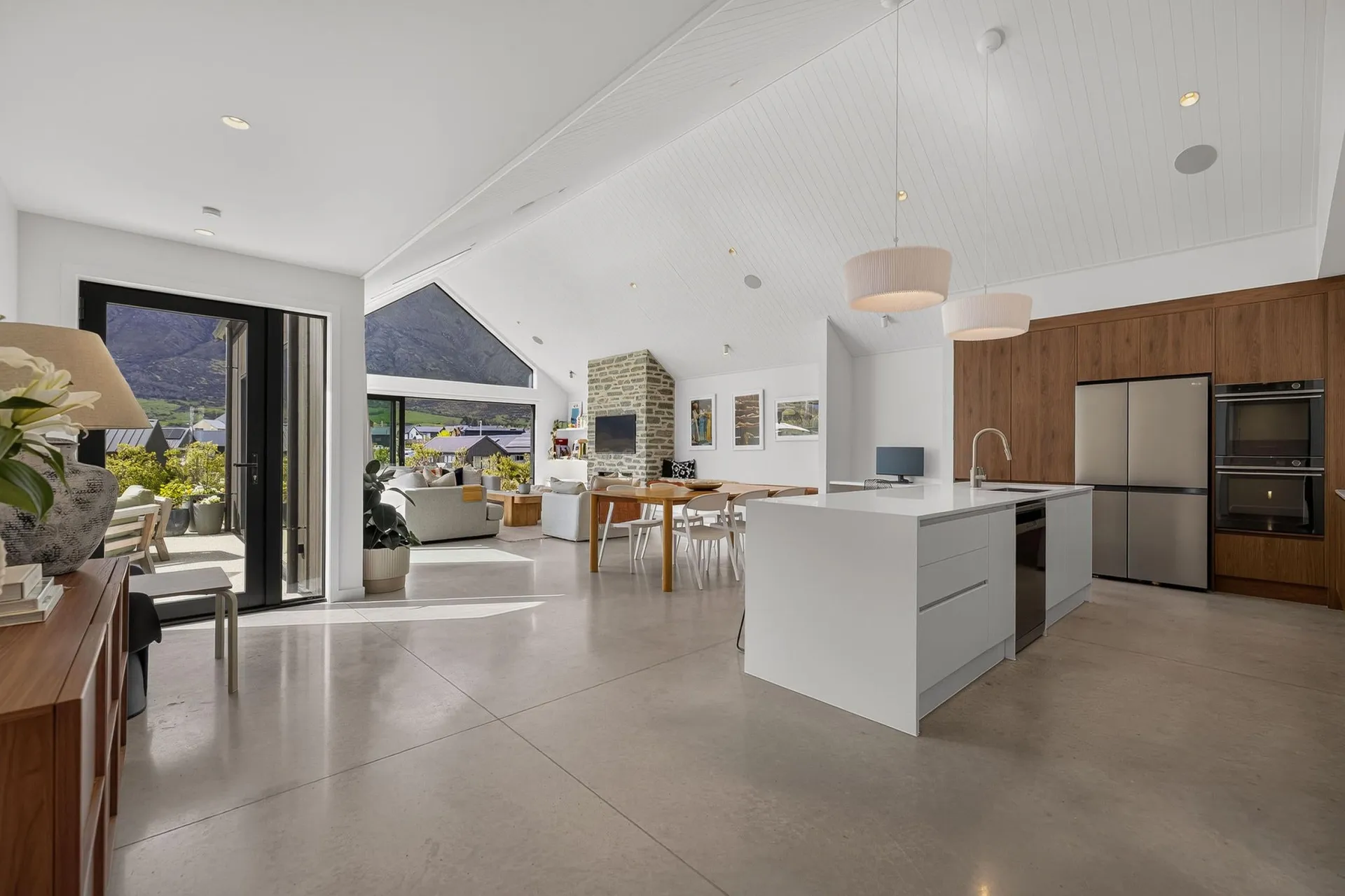 Open-plan view of a white island and timber-look tall cabinets beside the living area
