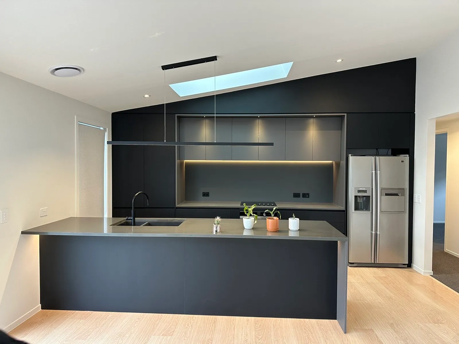 Charcoal island and tall cabinets with a lit recess under a skylight and linear pendant